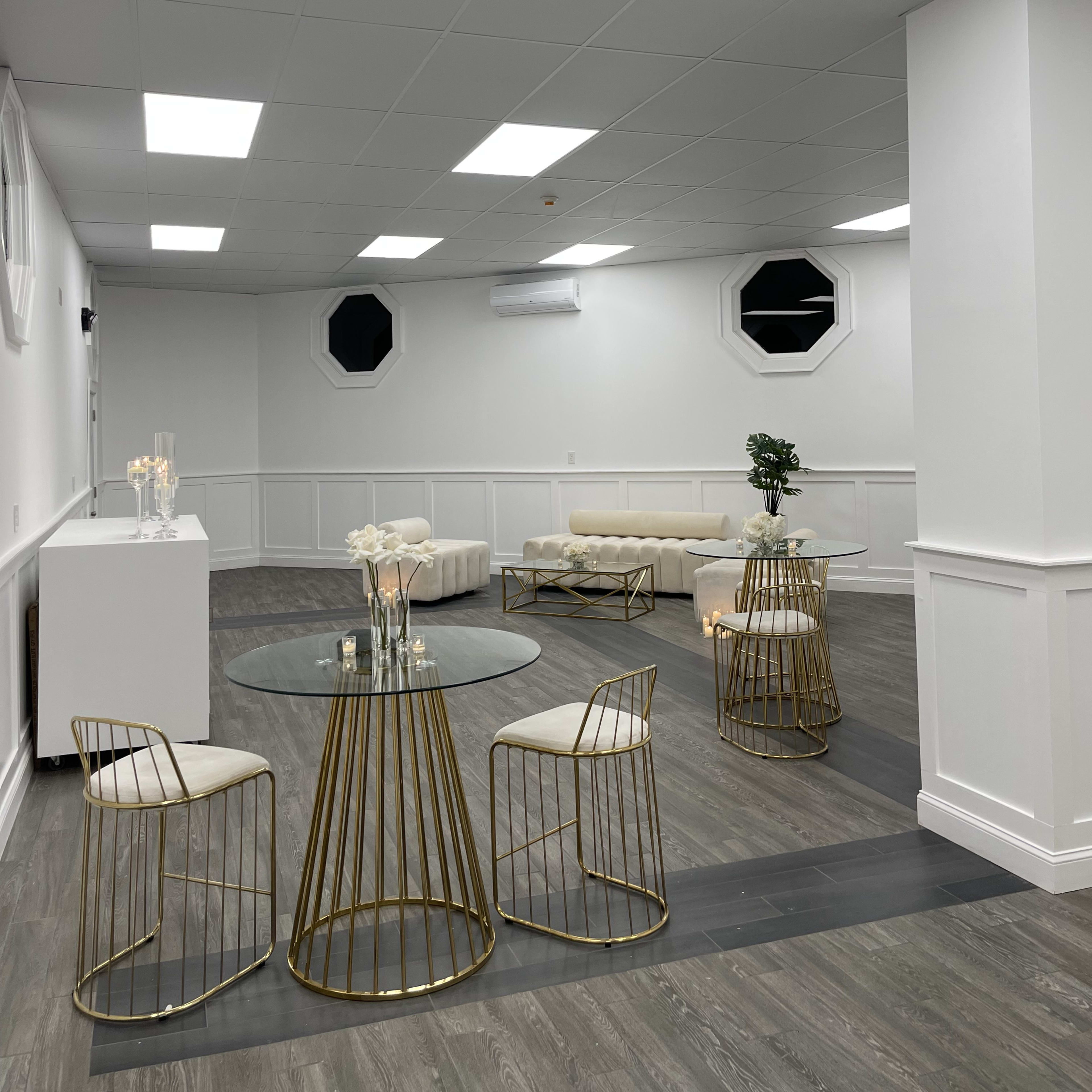 A modern, minimalistic interior space with white walls, a gray floor, and gold-accented furniture, including chairs and tables.