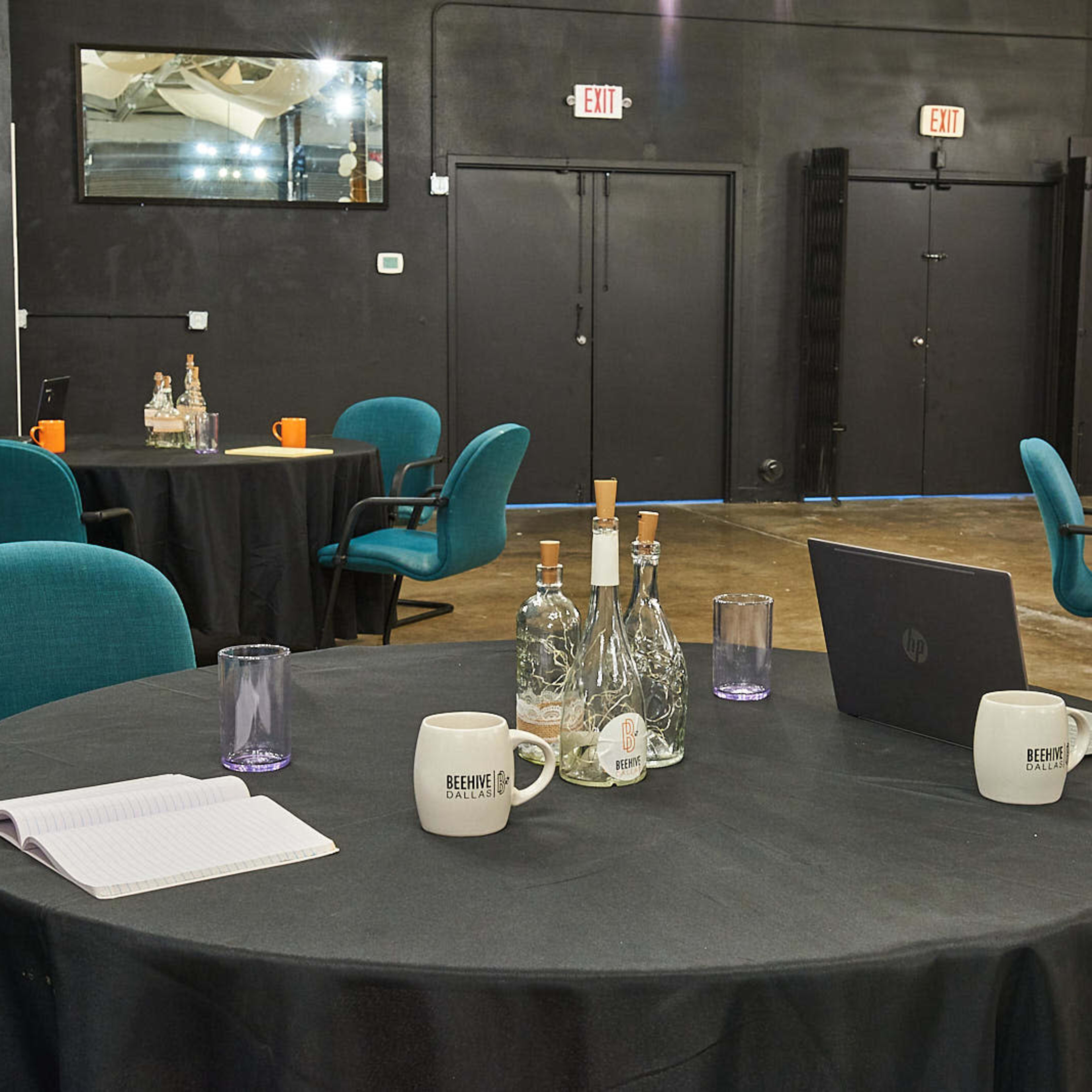 A conference room with round tables covered in black tablecloths, each equipped with chairs, bottles of water, and notebooks, all set for a meeting.
