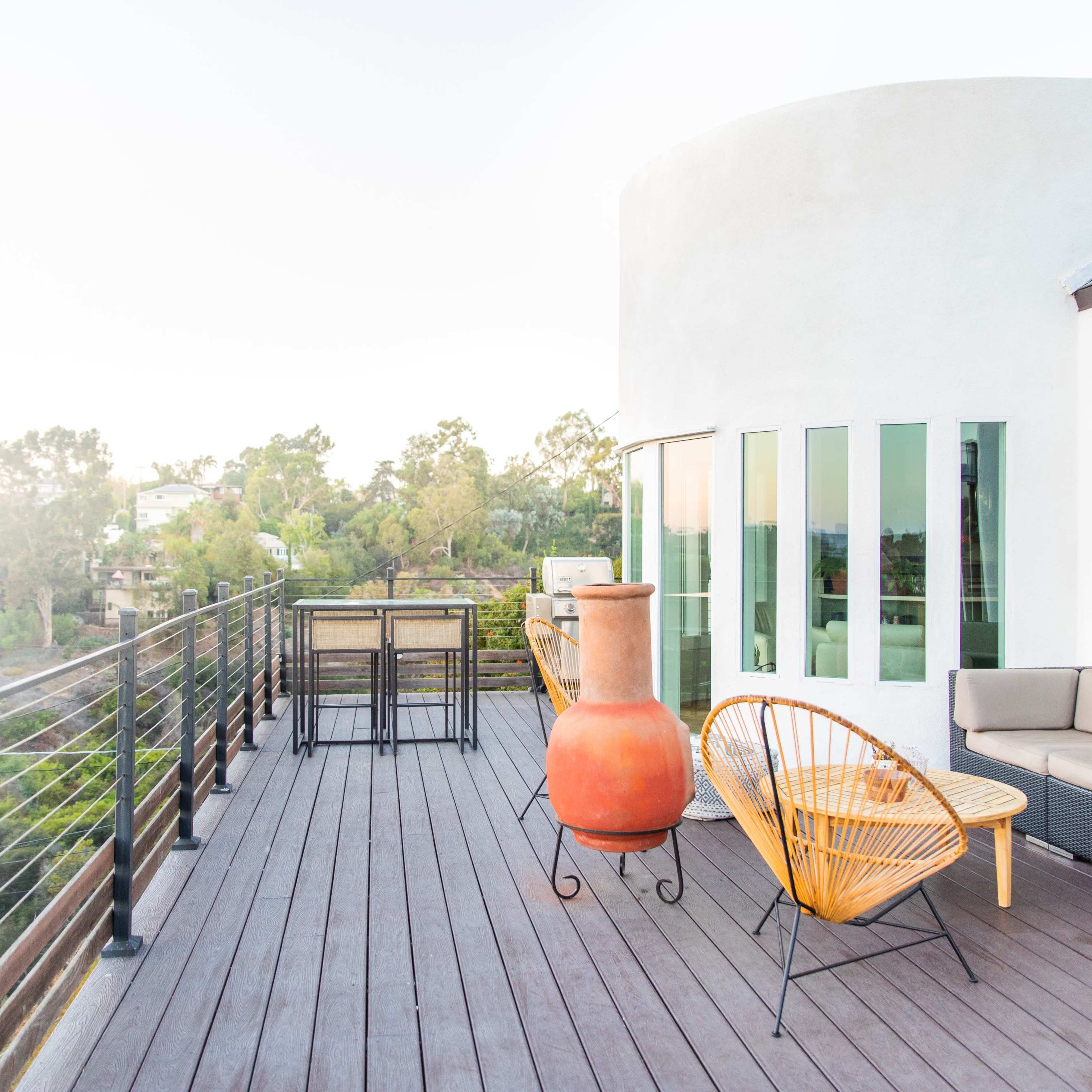 A modern rooftop terrace features a seating area, a large clay pot, and views of surrounding greenery.