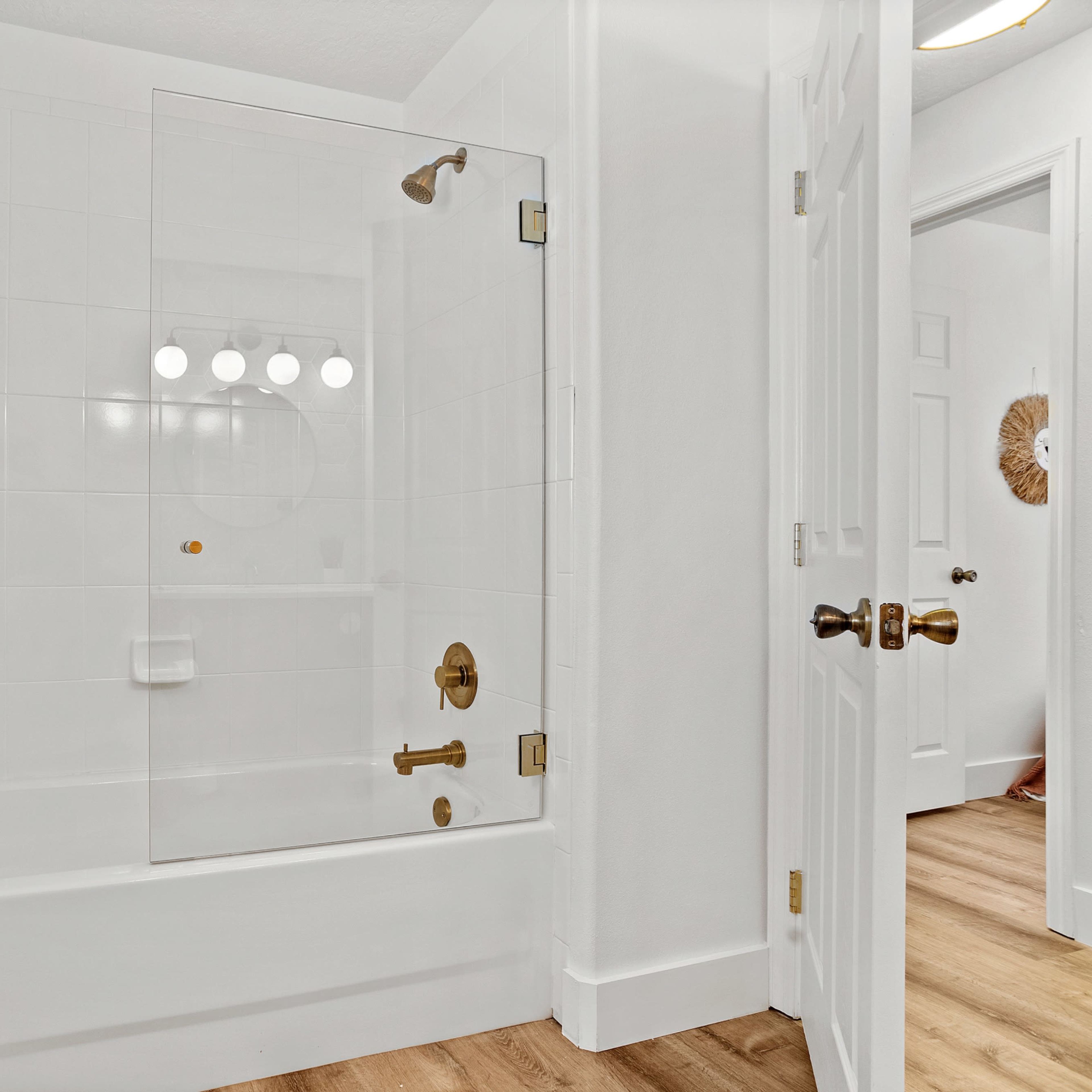 A modern bathroom featuring a glass shower enclosure next to a bathtub, with a wooden floor and white walls.