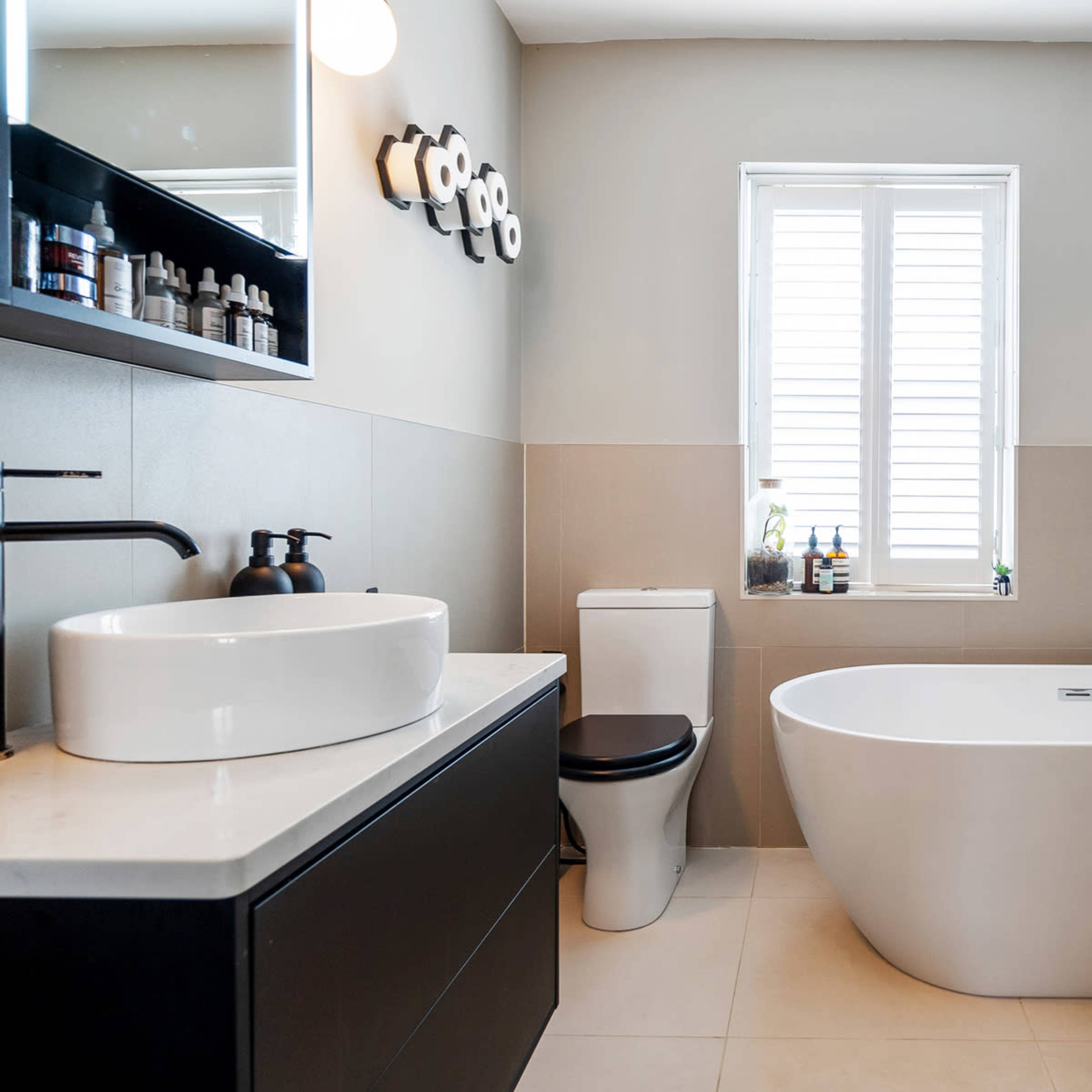 A modern bathroom featuring a freestanding bathtub, a sink with a black faucet, and natural light coming through a window.