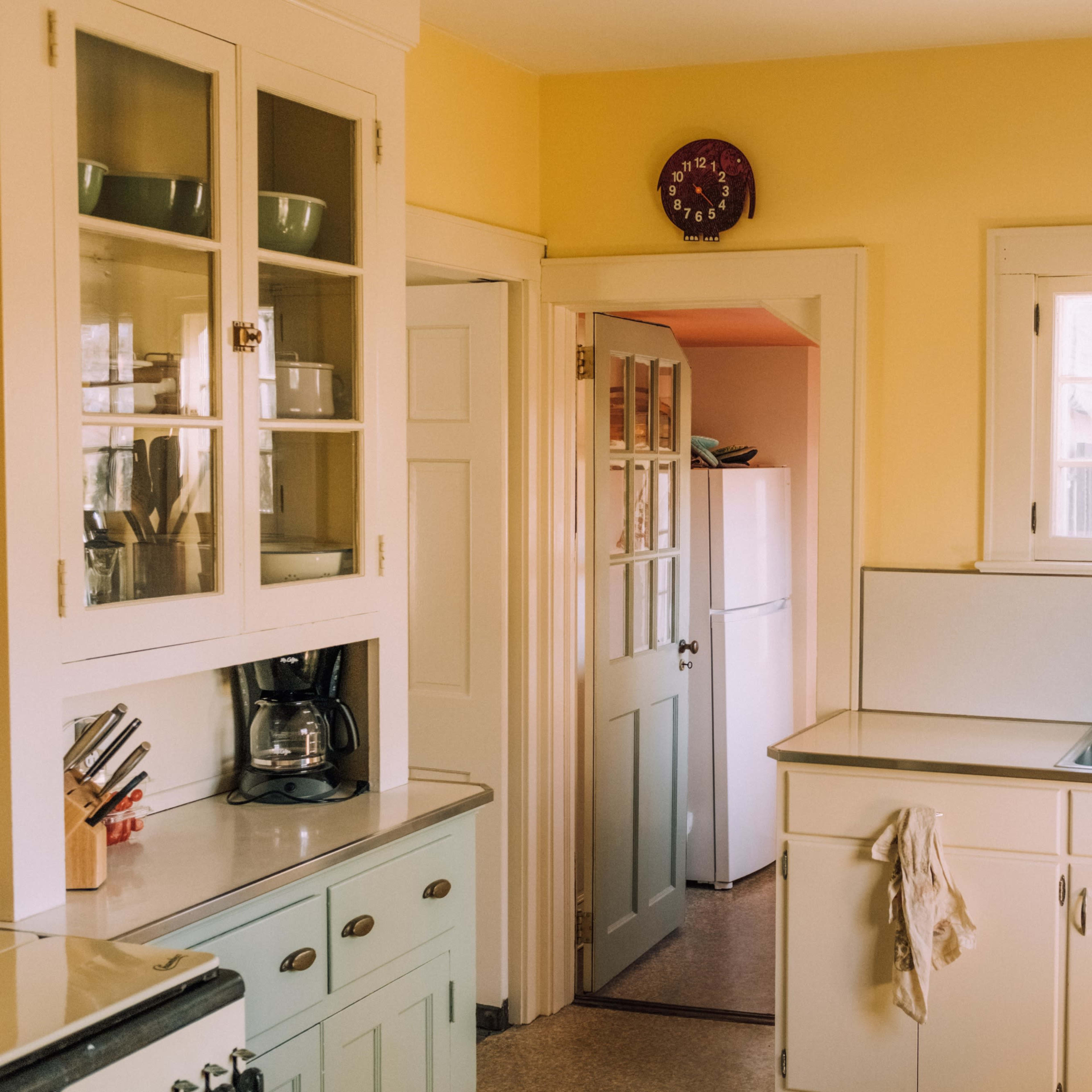 A bright kitchen with yellow walls, equipped with cabinets, a sink, and an open door leading to another room.