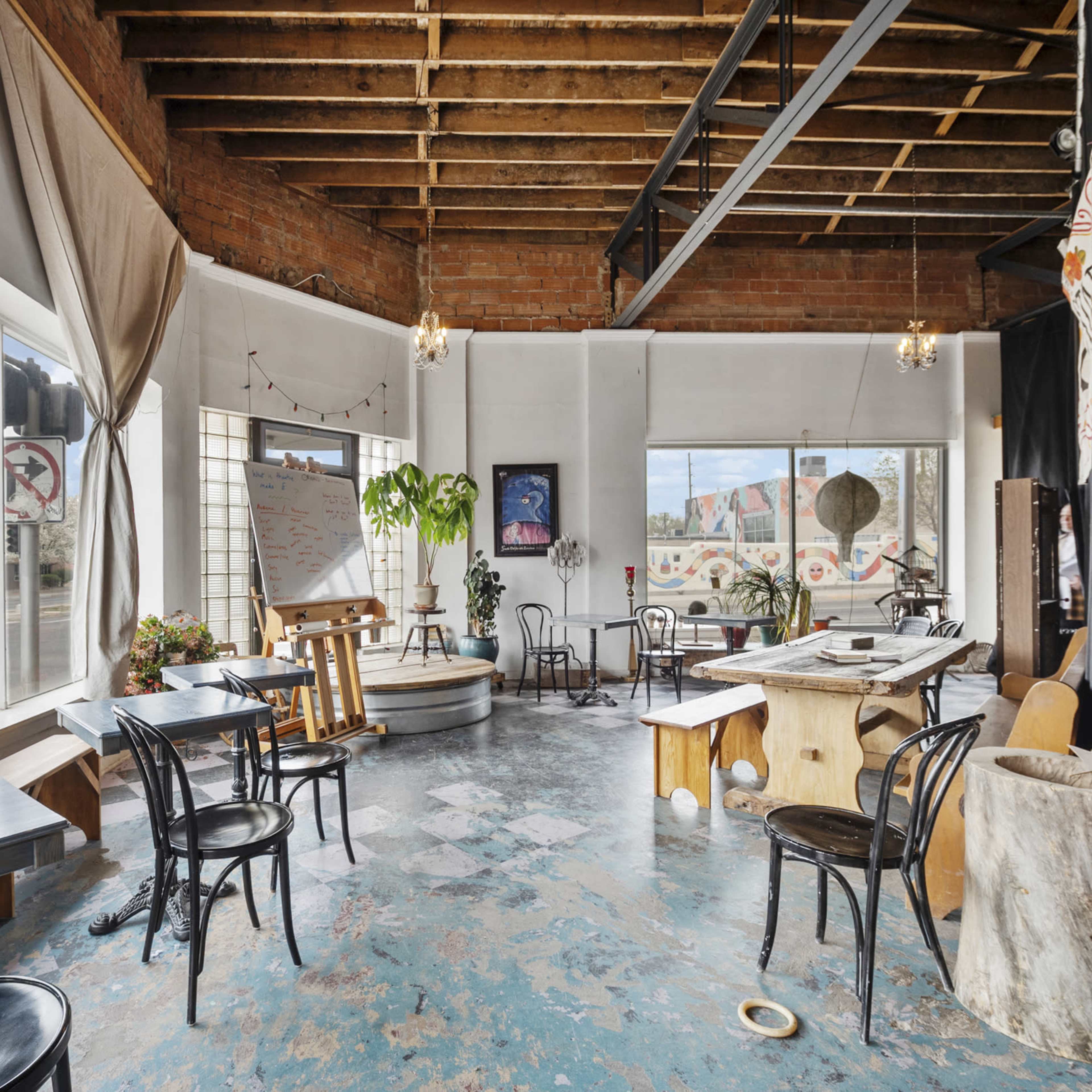 A spacious café interior with wooden tables and chairs, large windows, and exposed brick walls.