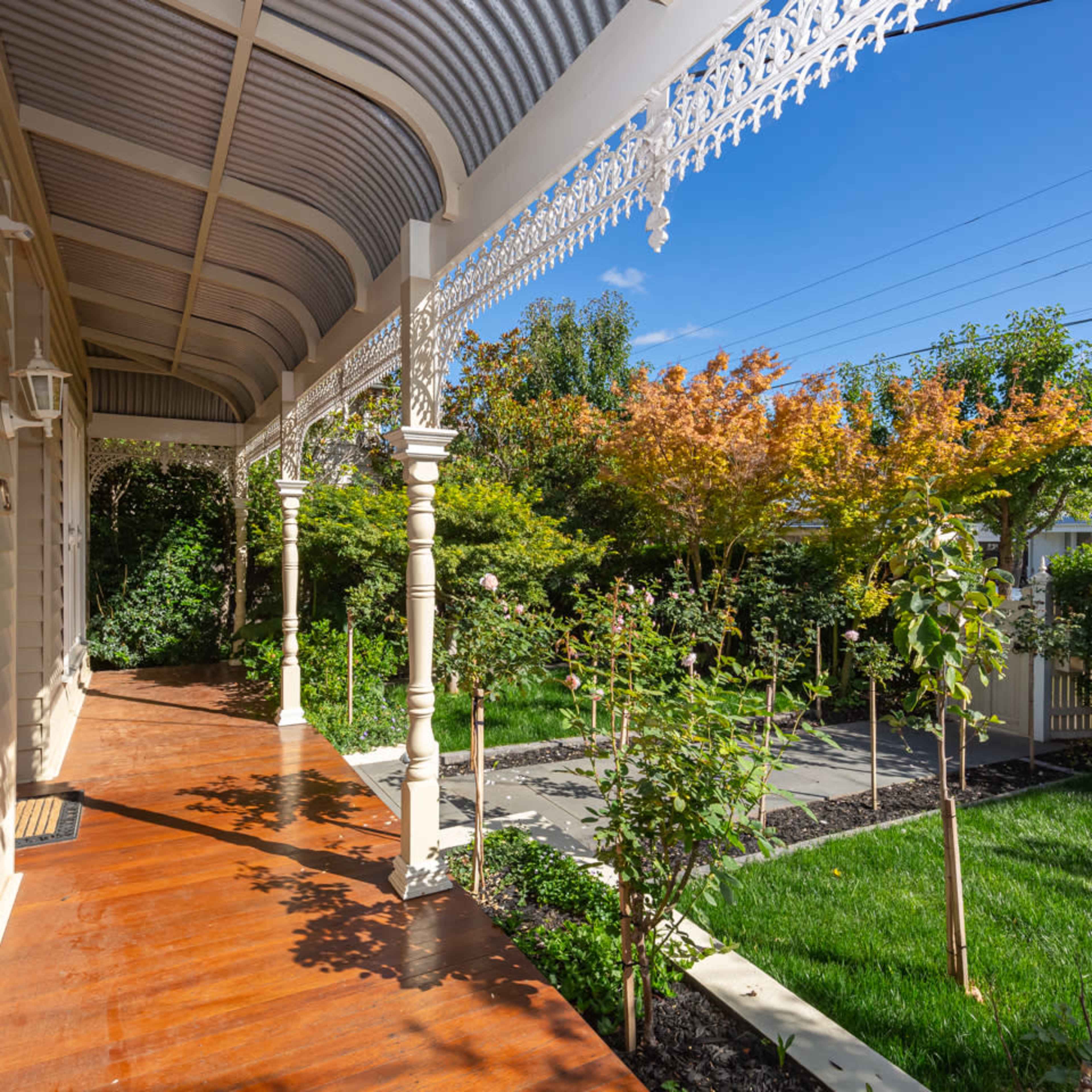 A porch with decorative pillars and an expansive yard featuring various trees and shrubs under a clear blue sky.