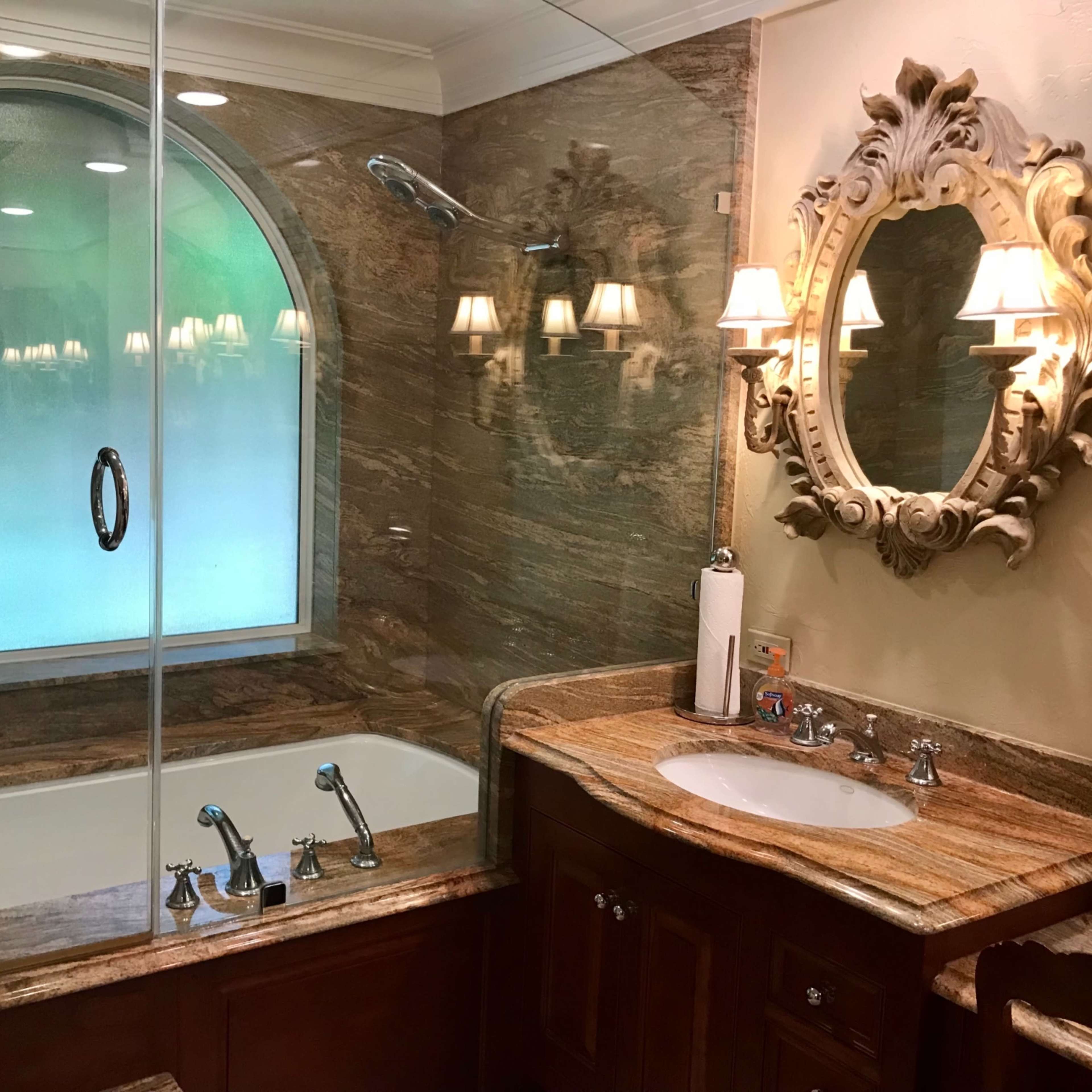A bathroom with a glass shower enclosure, a large bathtub, a sink with faucets, and decorative lighting fixtures.