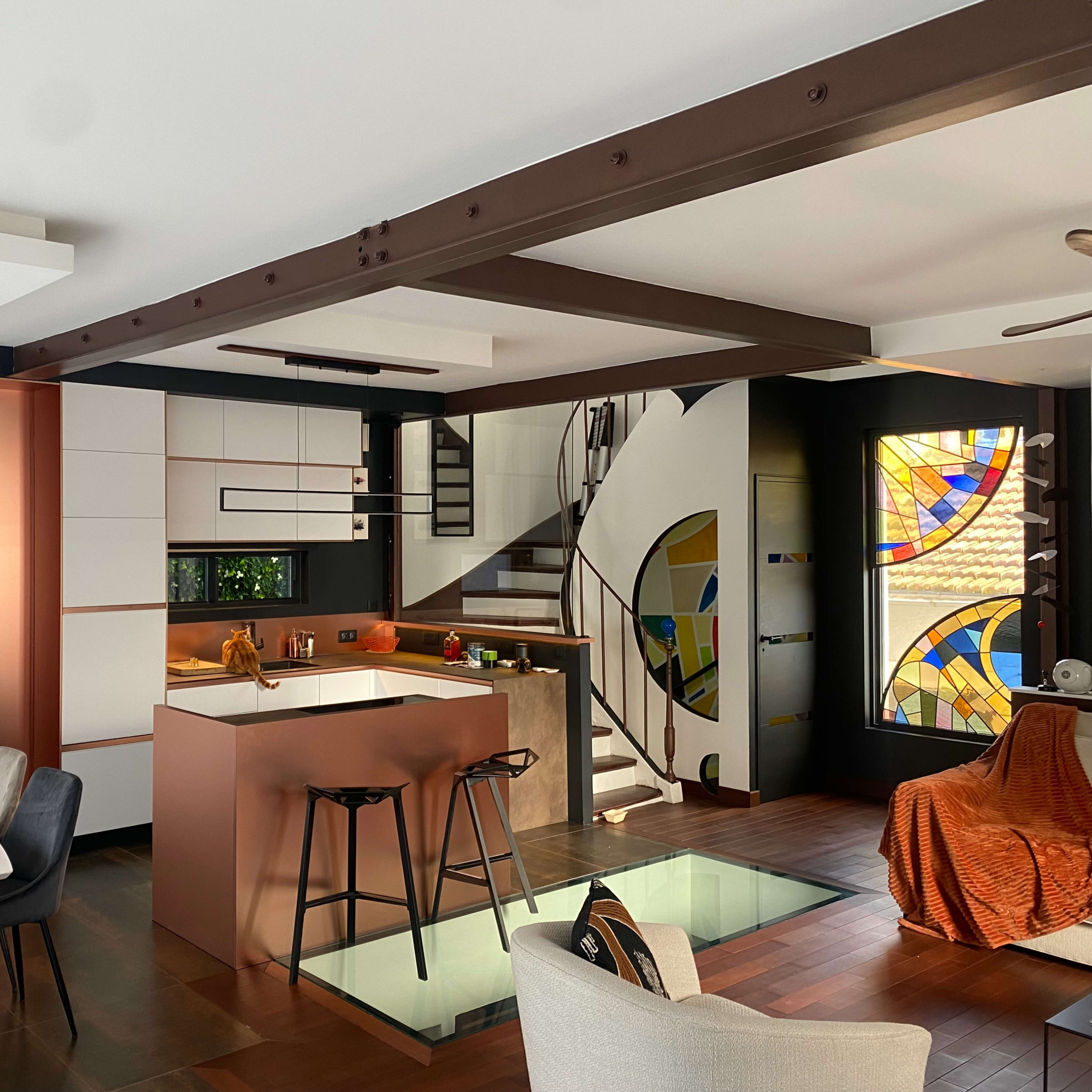 A modern kitchen and dining area featuring a glass floor, a spiral staircase, and a stained glass window.