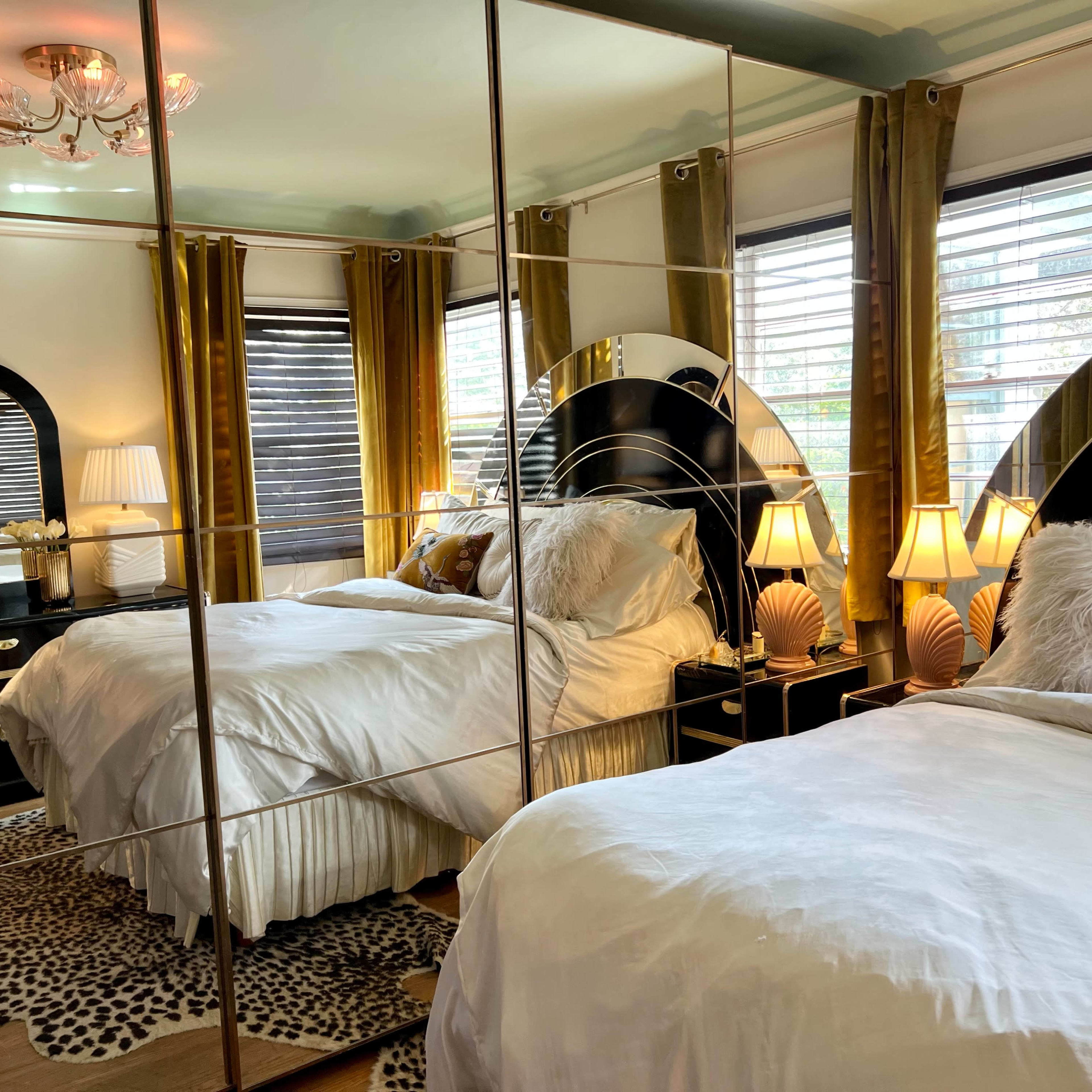 A decorated bedroom with mirrored closet doors, two beds with white bedding, and elegant lighting fixtures.
