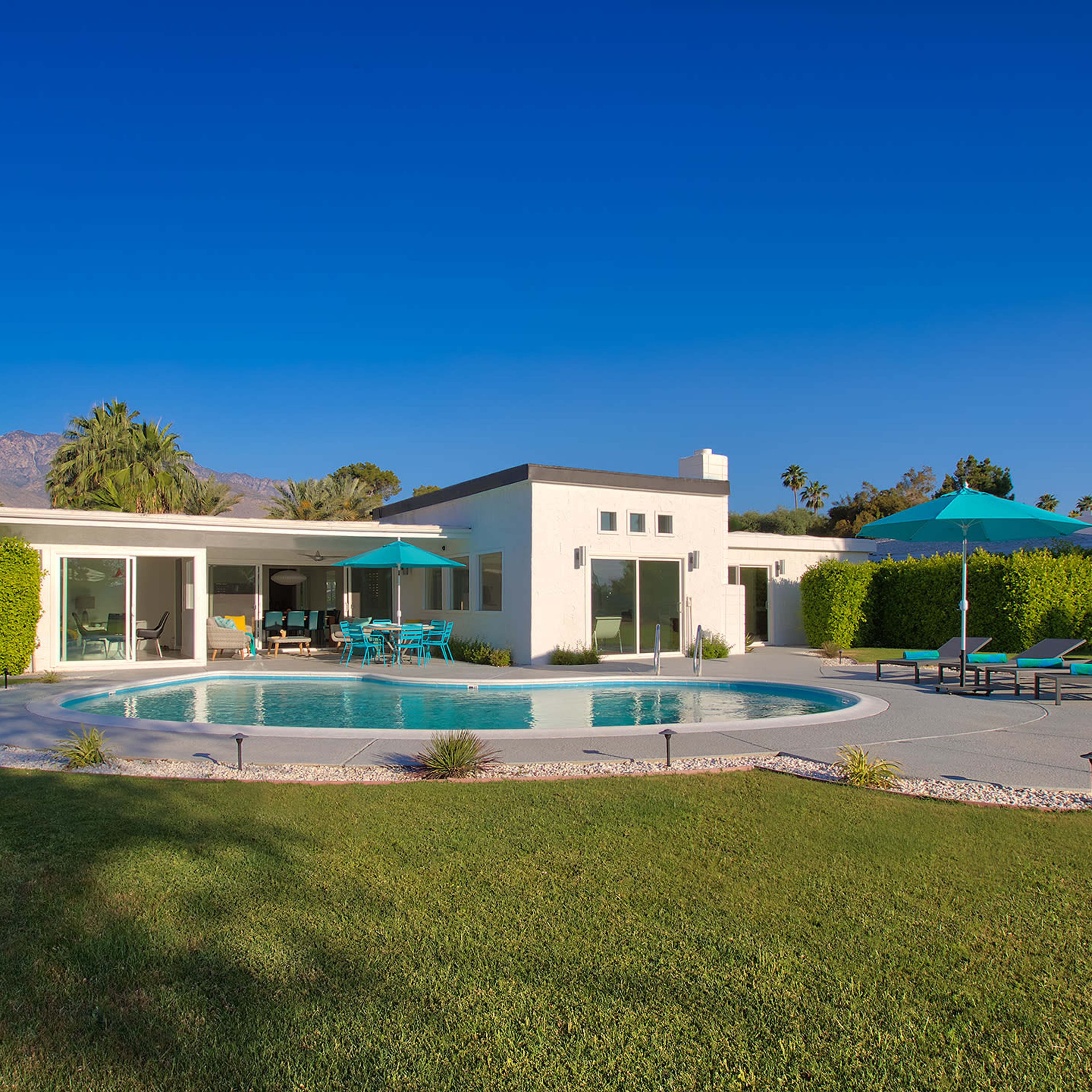 A modern residential home features a circular swimming pool surrounded by lounge chairs and palm trees against a clear blue sky.