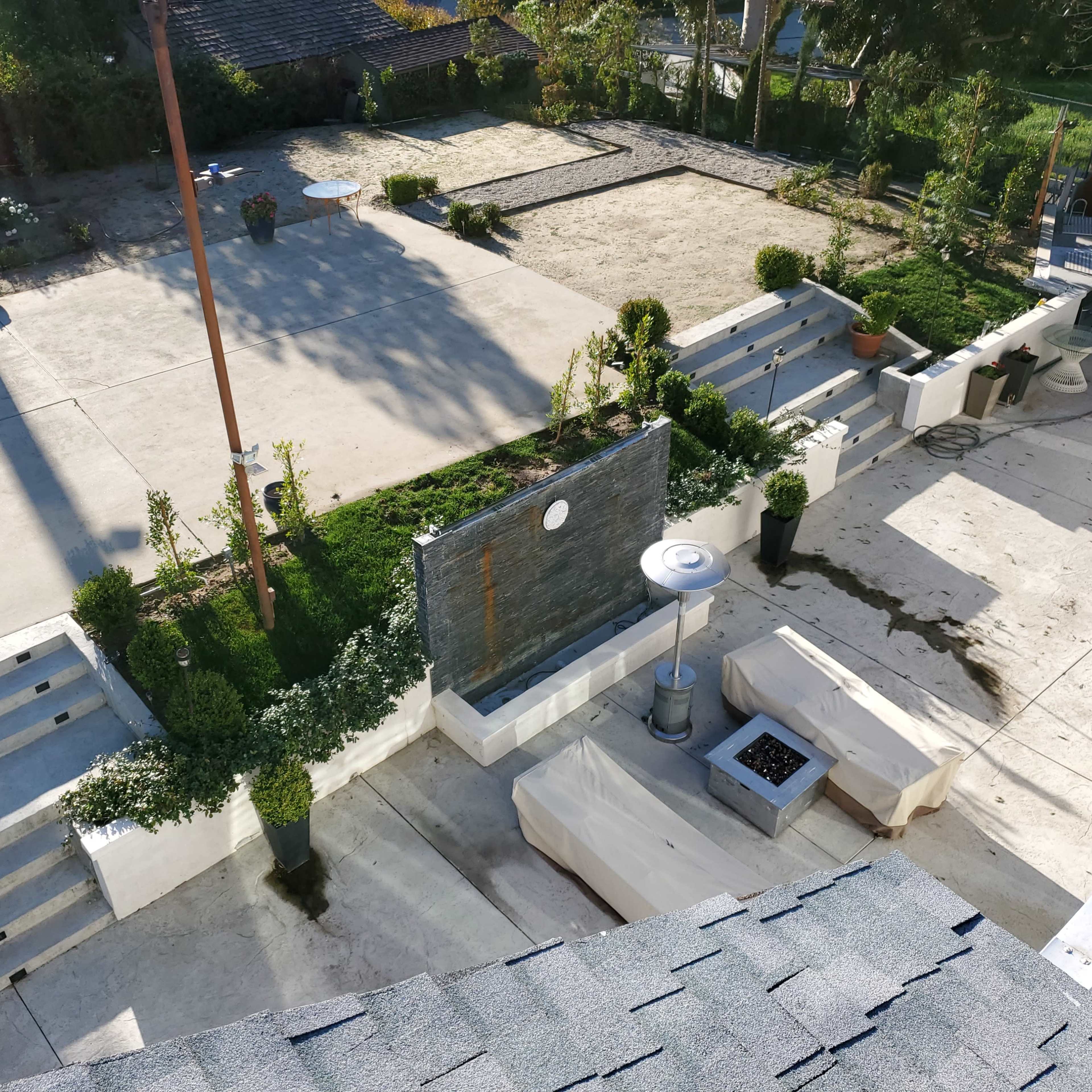 A landscaped outdoor area with concrete pathways, planter boxes, a fire pit, and a large sandy space in the center.