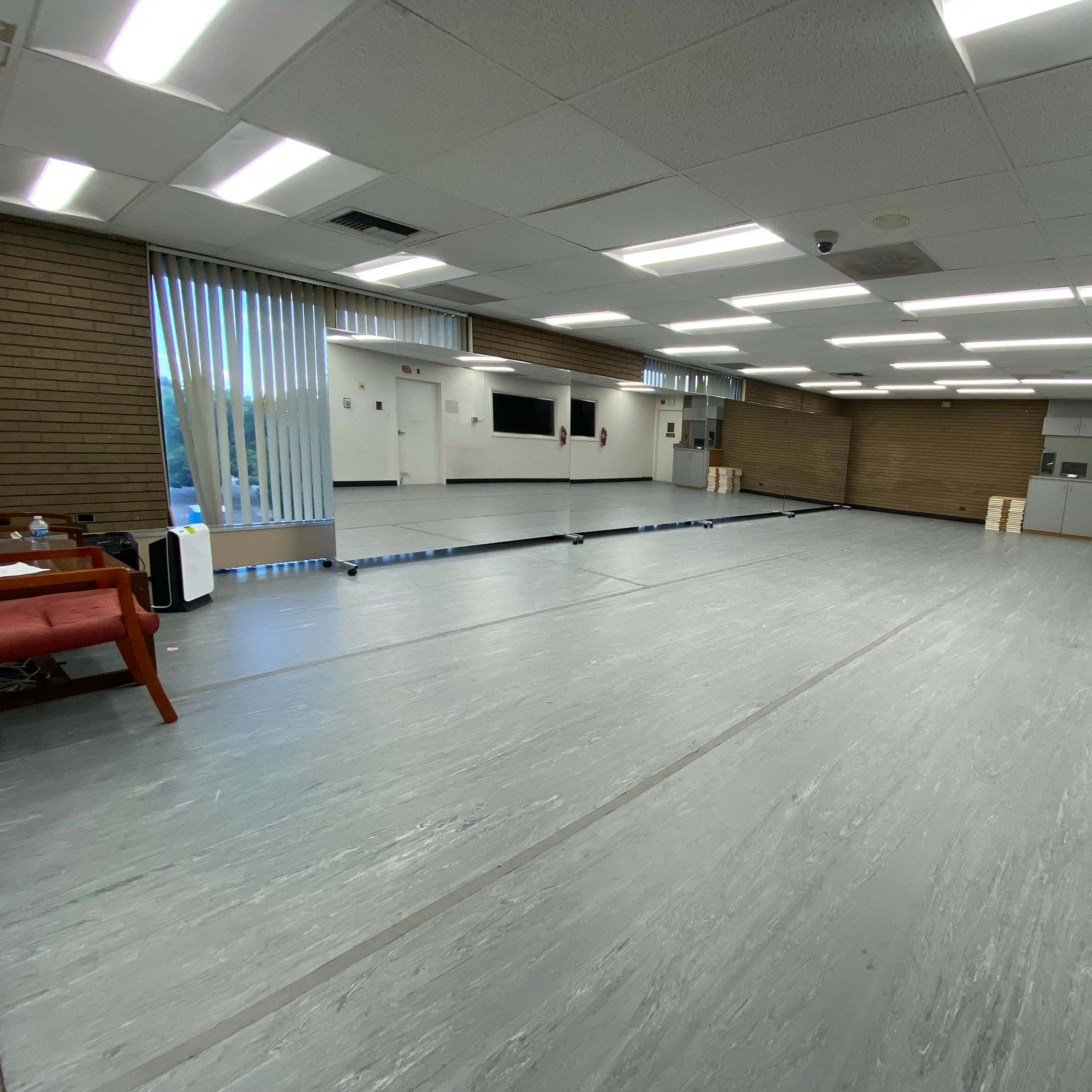 A spacious, well-lit interior room with a smooth gray floor, large windows, and a few pieces of furniture.
