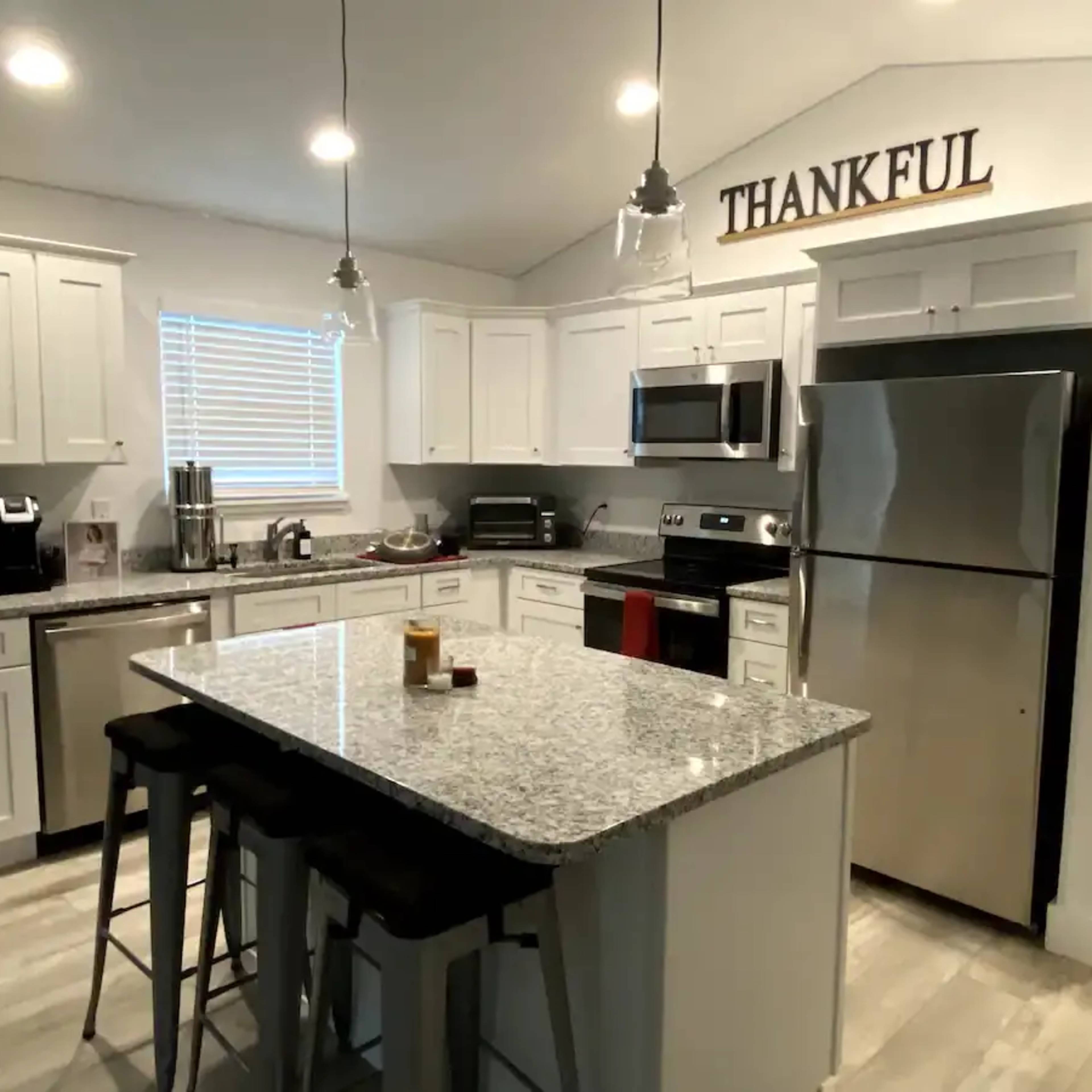 A modern kitchen features white cabinetry, stainless steel appliances, a granite countertop, and seating at a central island.