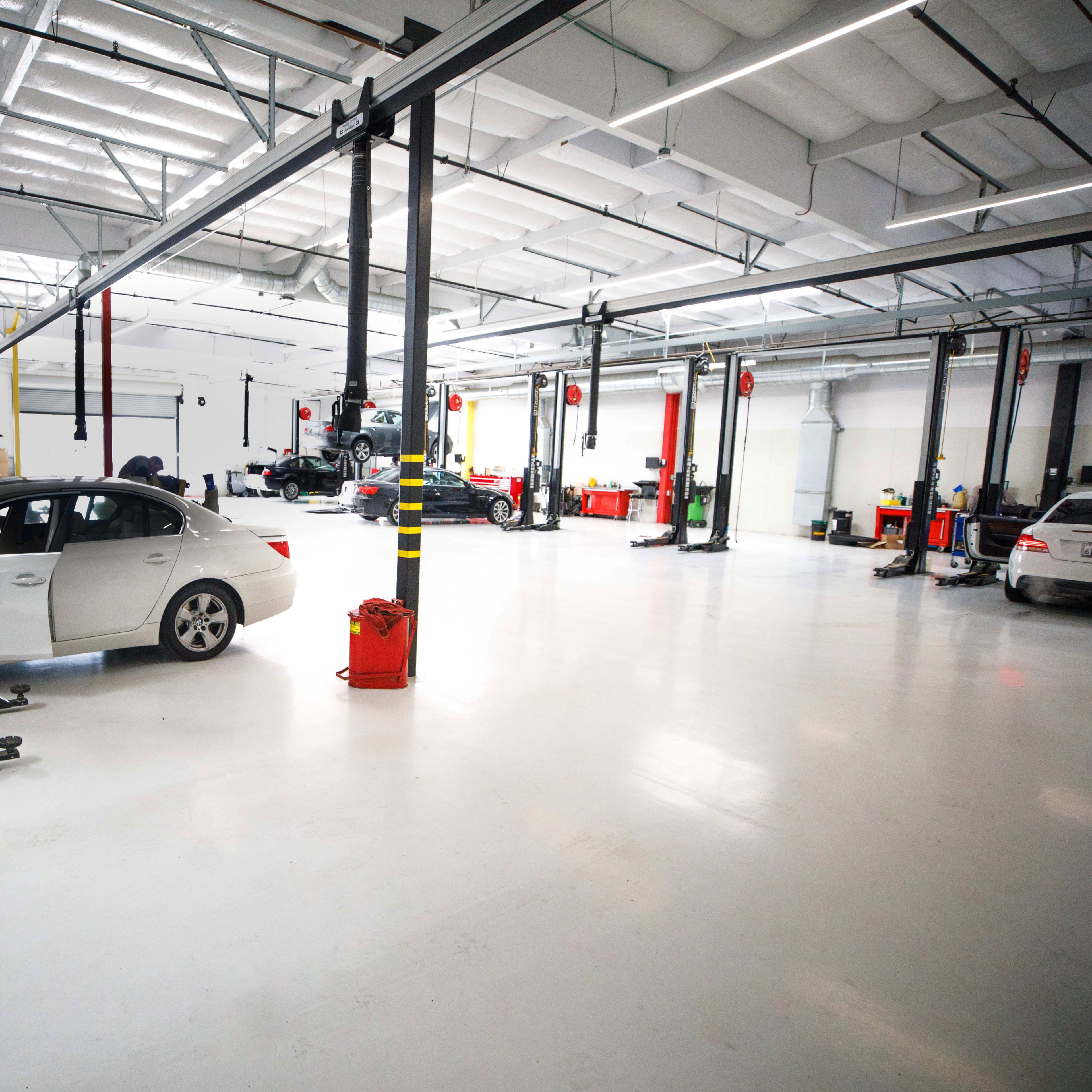 A spacious automotive repair shop with several cars on raised lifts and various tools and equipment organized around the area.