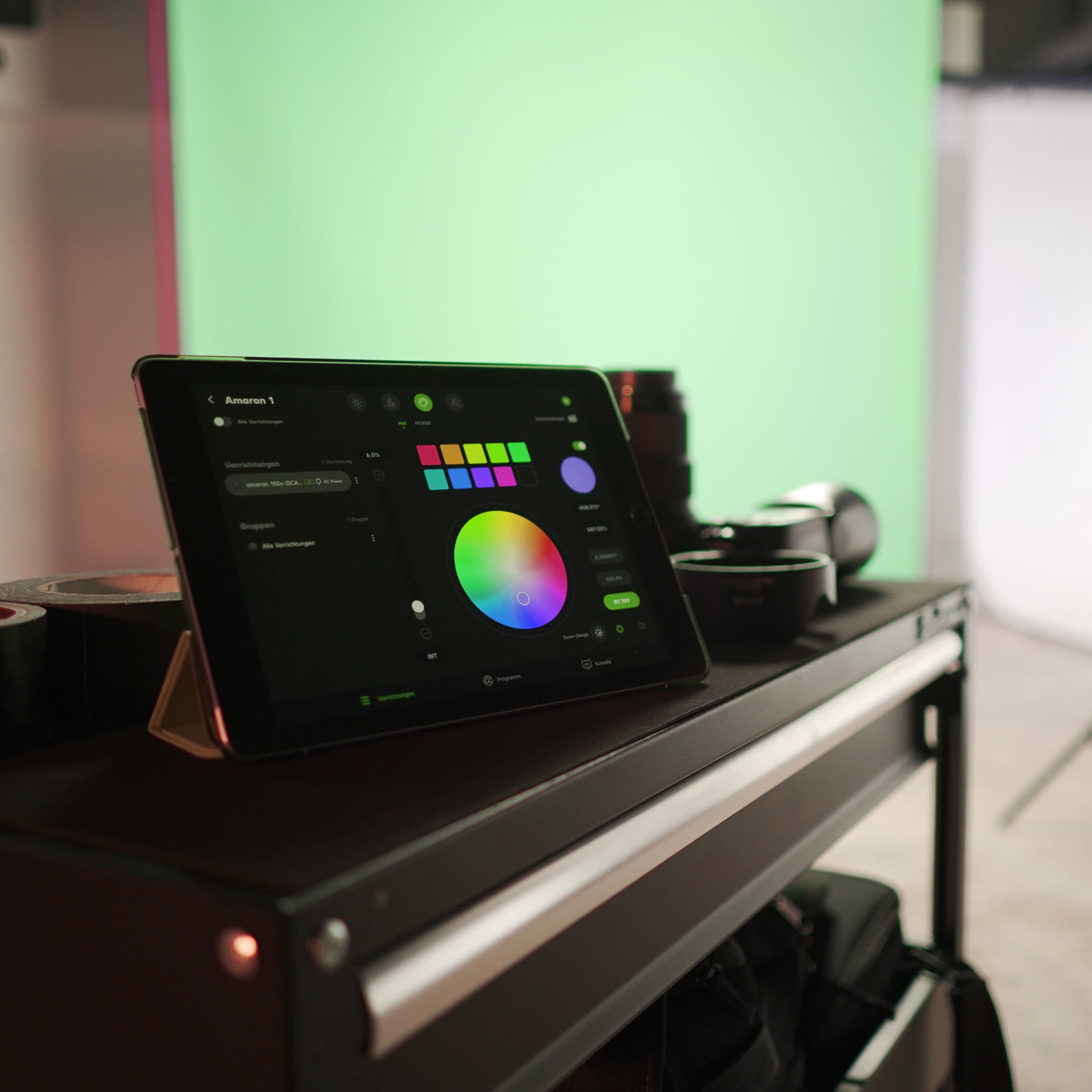 An iPad displaying a color selection interface rests on a cart in a studio with green and white backdrop setups.