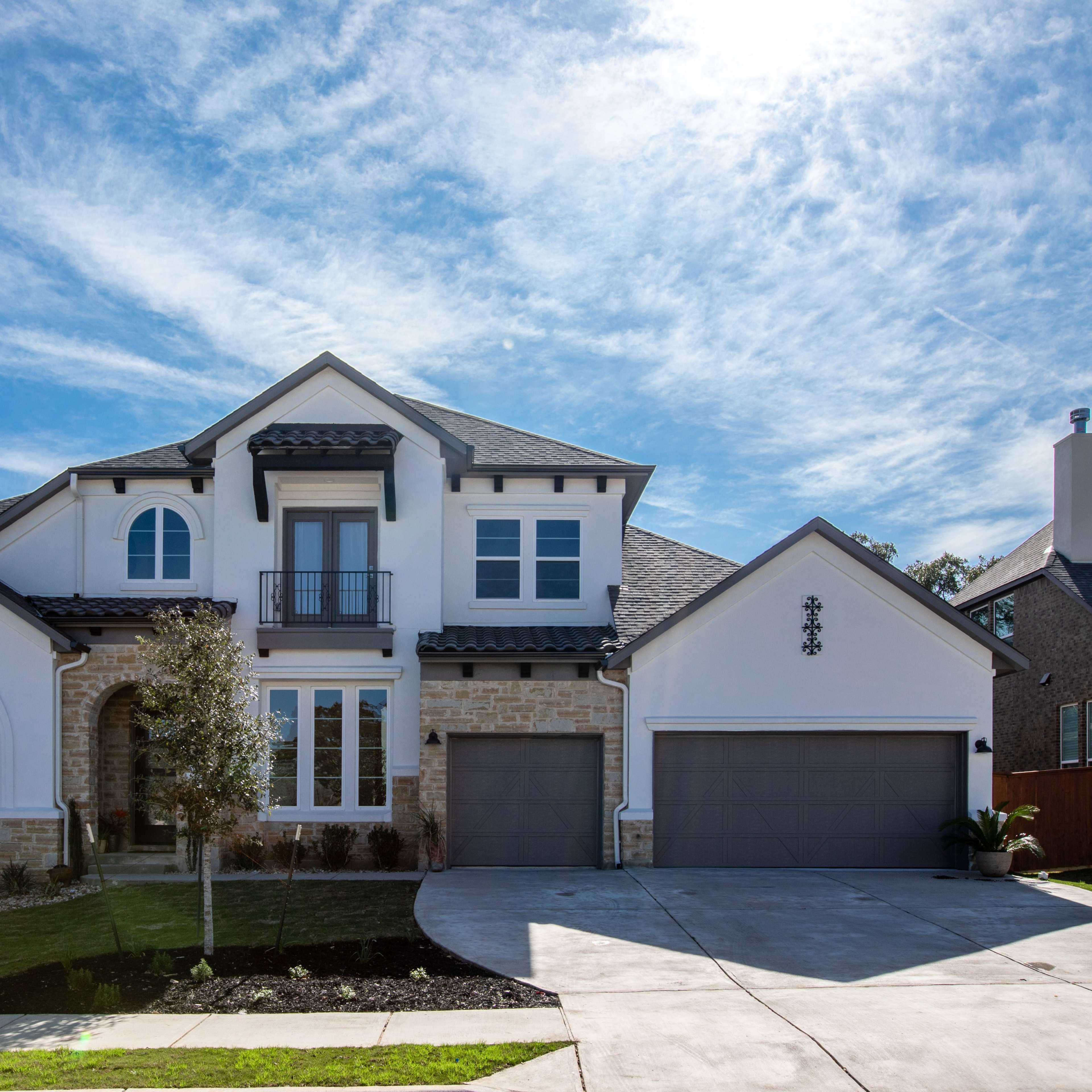 A two-story house with a stone and stucco exterior features a front lawn, a circular driveway, and large windows.