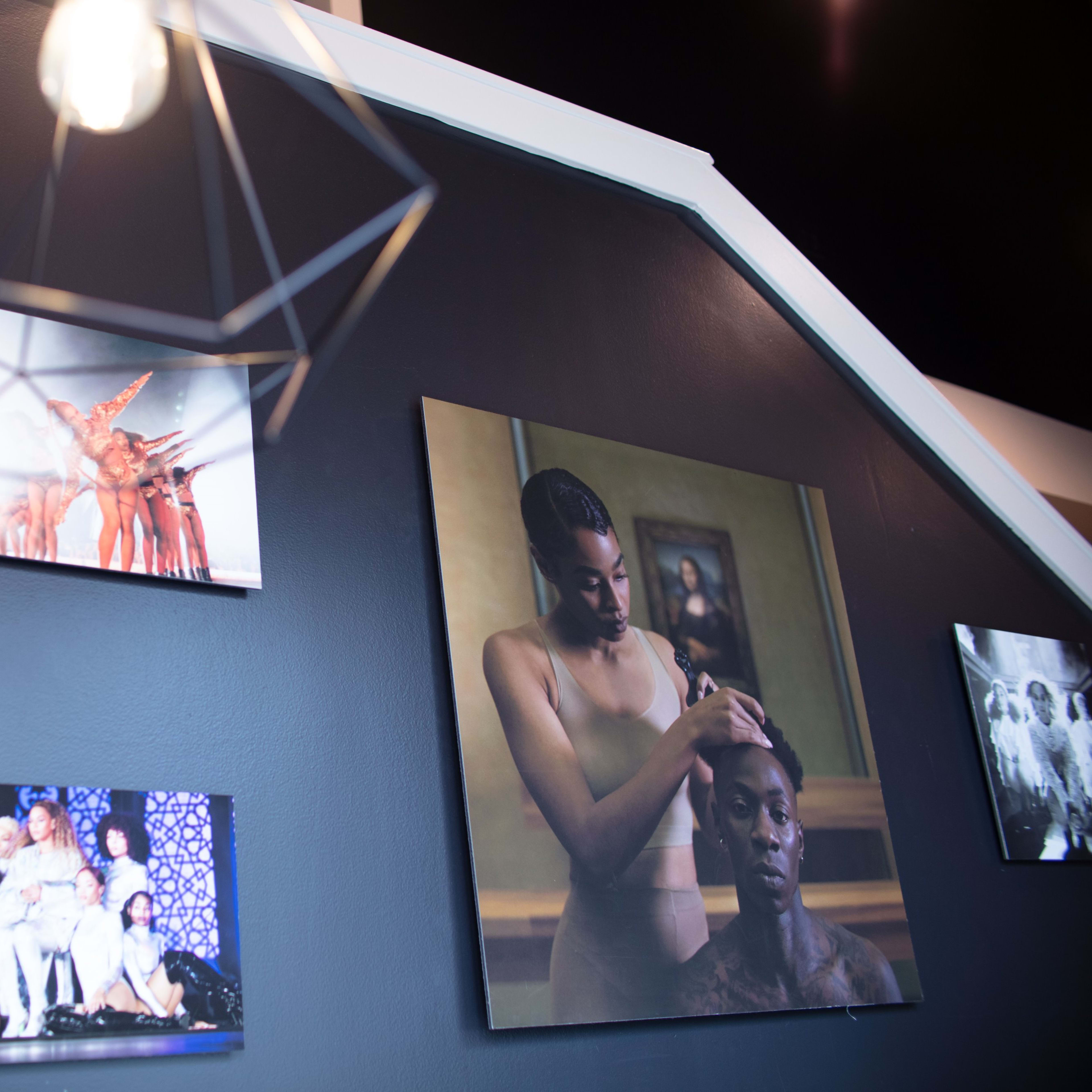 A black wall adorned with various framed photographs and a geometric pendant light hanging above.
