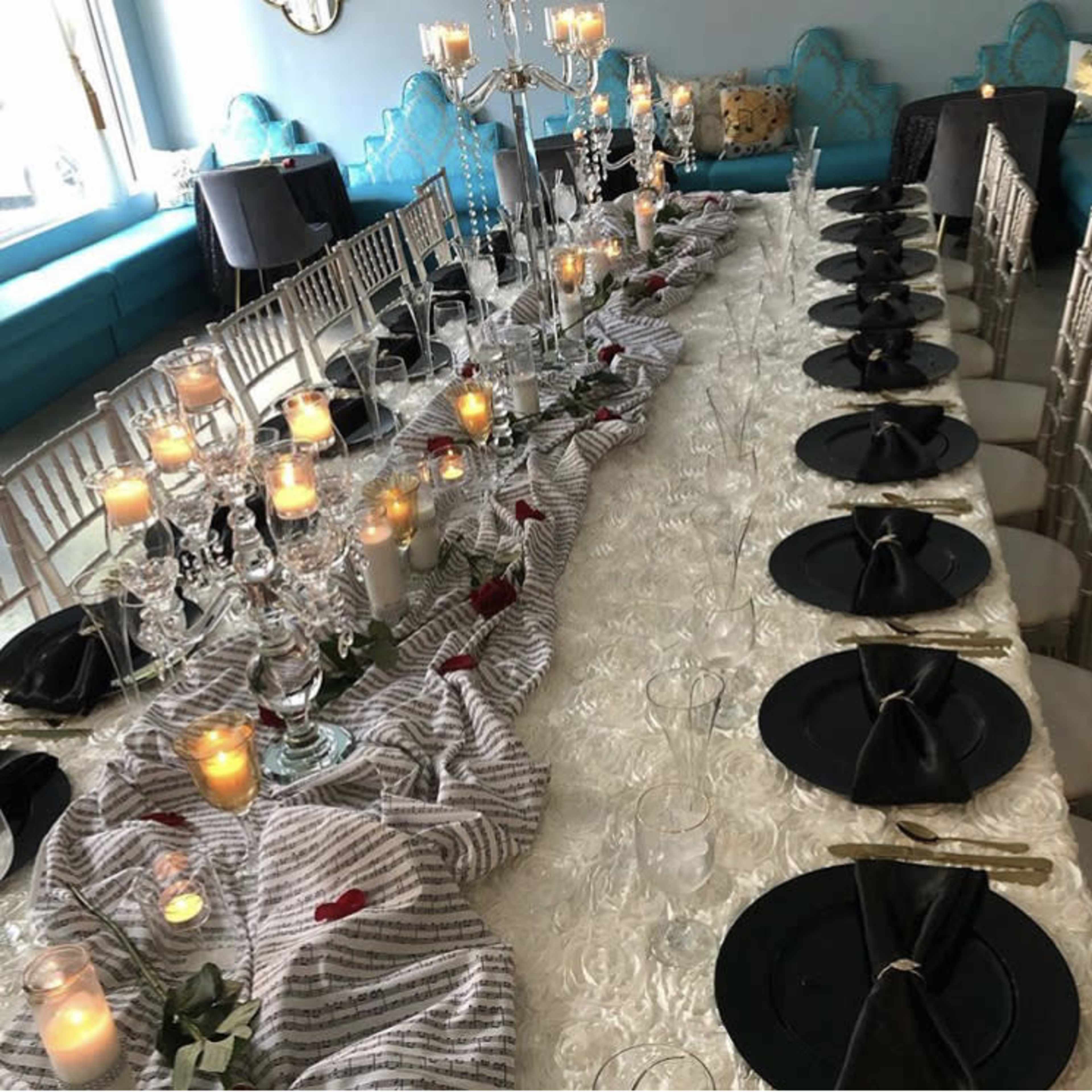A long dining table is set with black plates, glassware, and candles, adorned with a striped cloth and decorative centerpieces.