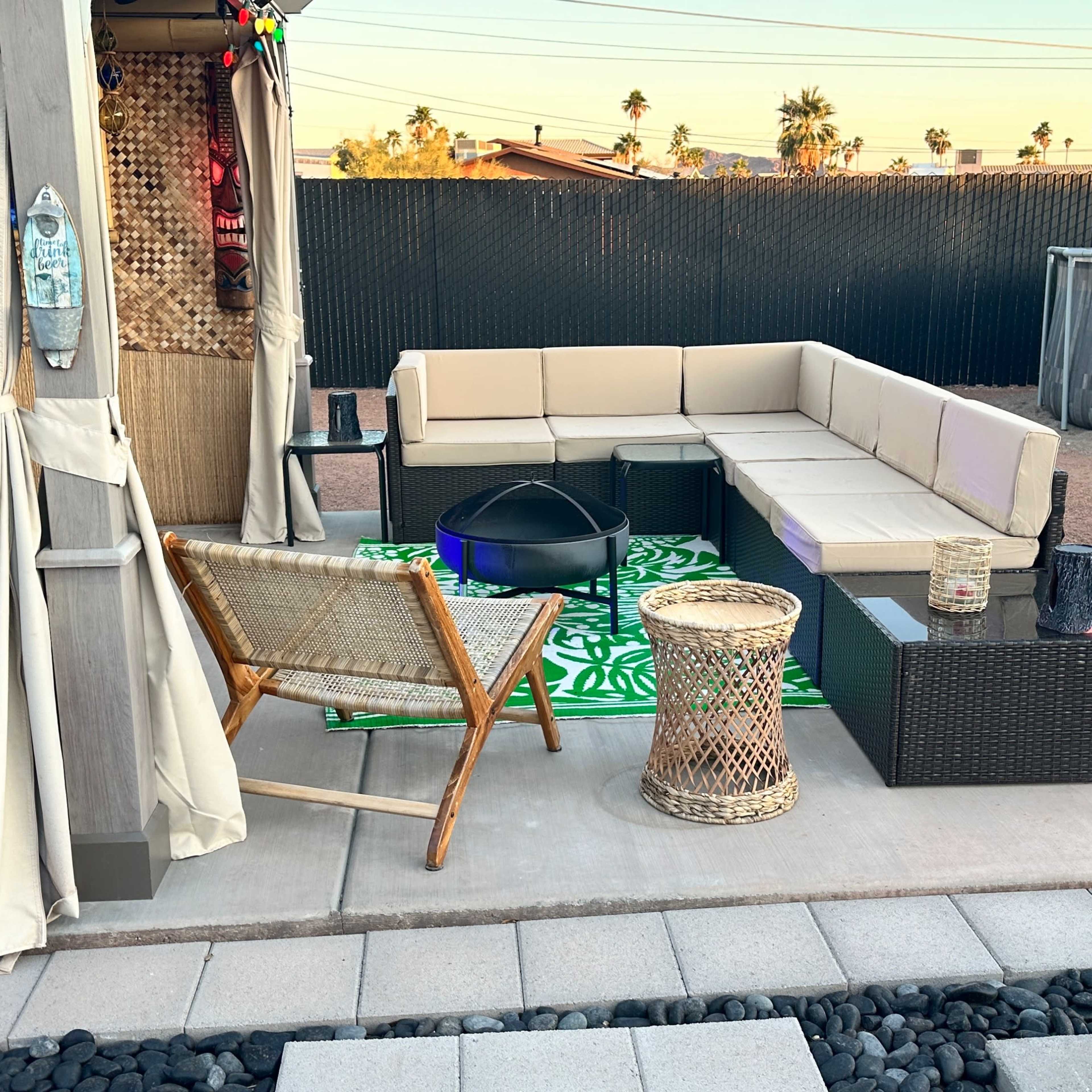 A patio area features a sectional sofa, a small table, and decorative elements like a flamingo and a fire pit surrounded by stone paving.