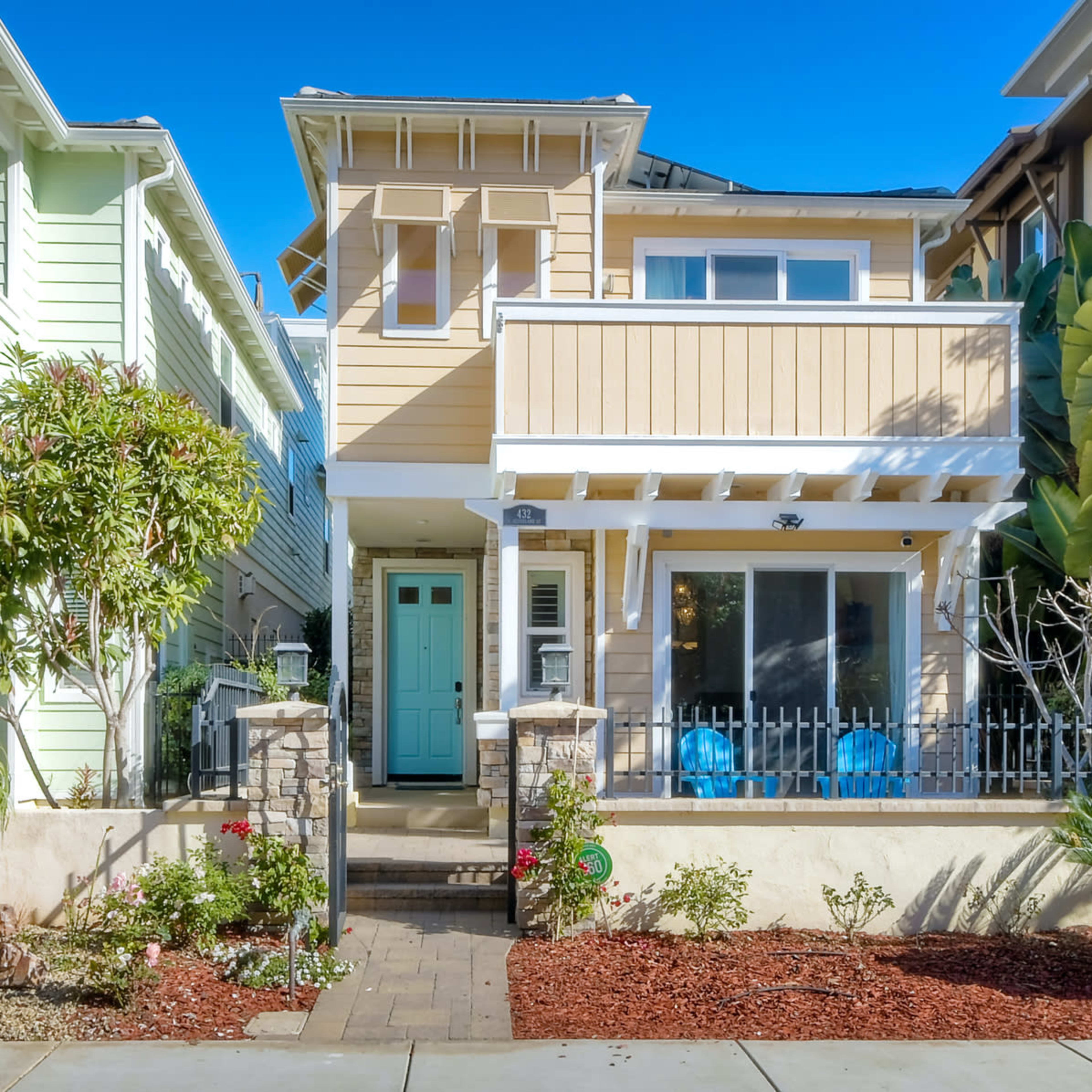 A two-story house with a pale yellow exterior, a front porch, and a green door, located in a neighborhood with similar homes.