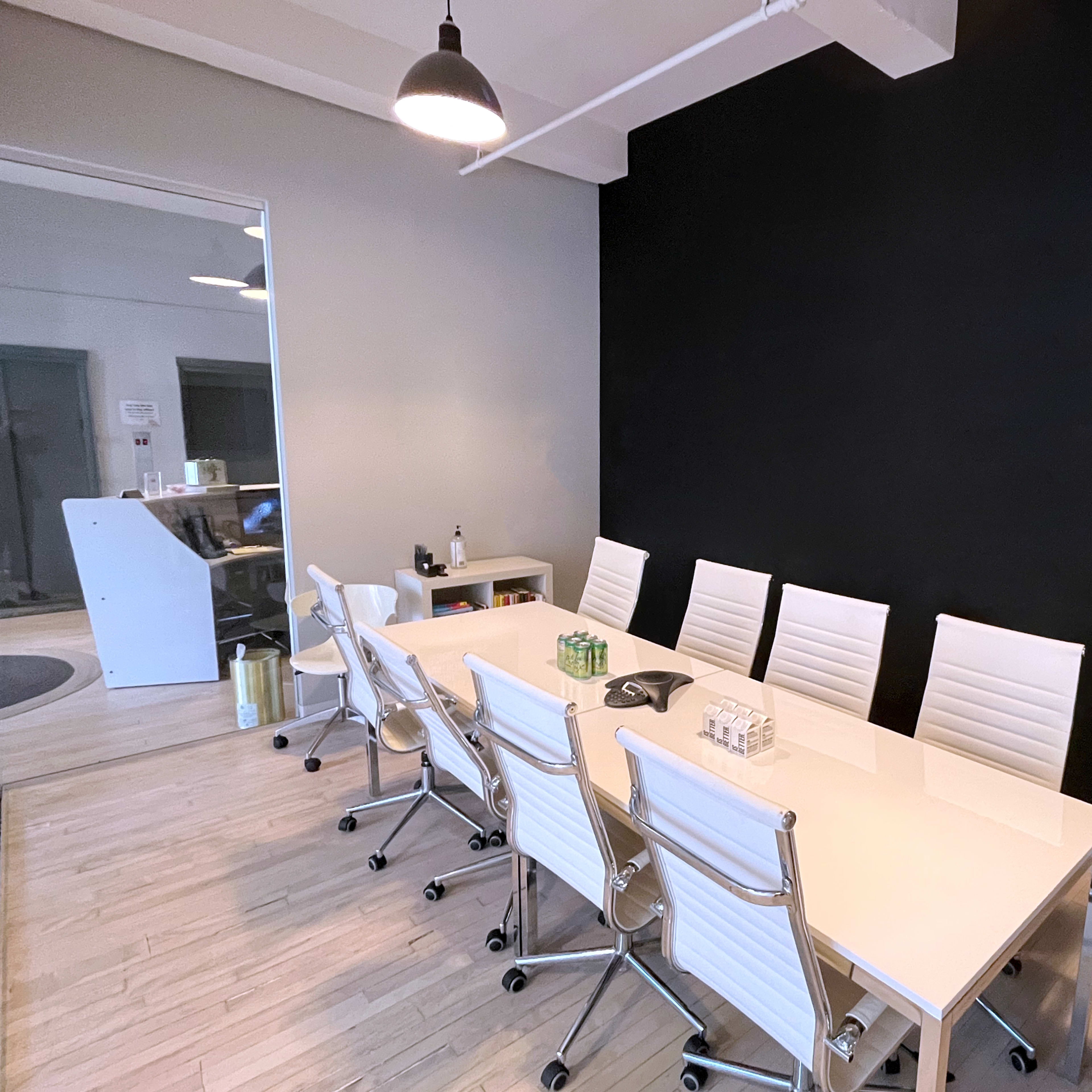 A modern conference room with a long white table surrounded by eight white chairs against a black accent wall.