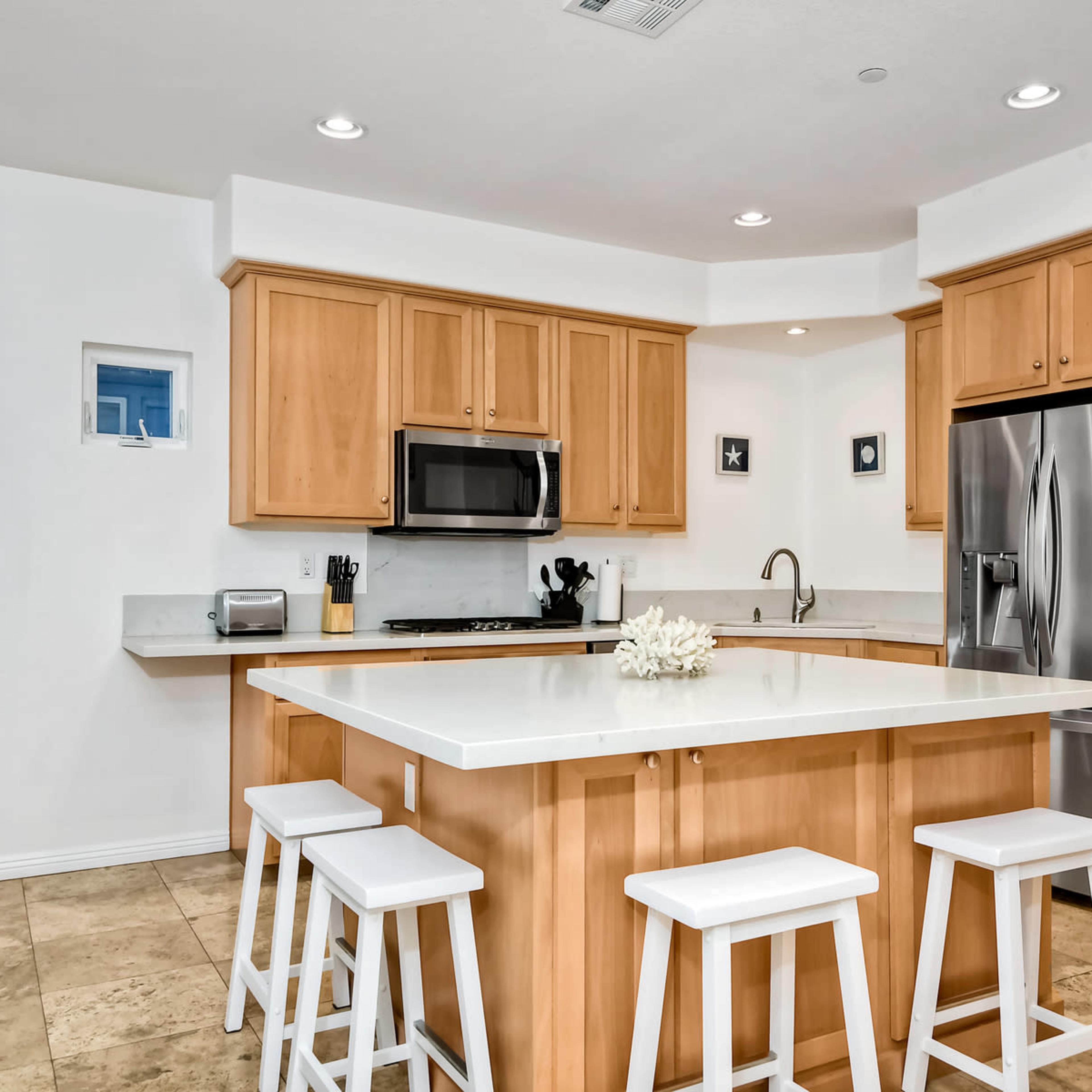 A modern kitchen with wooden cabinets, stainless steel appliances, and a central island with four white stools.