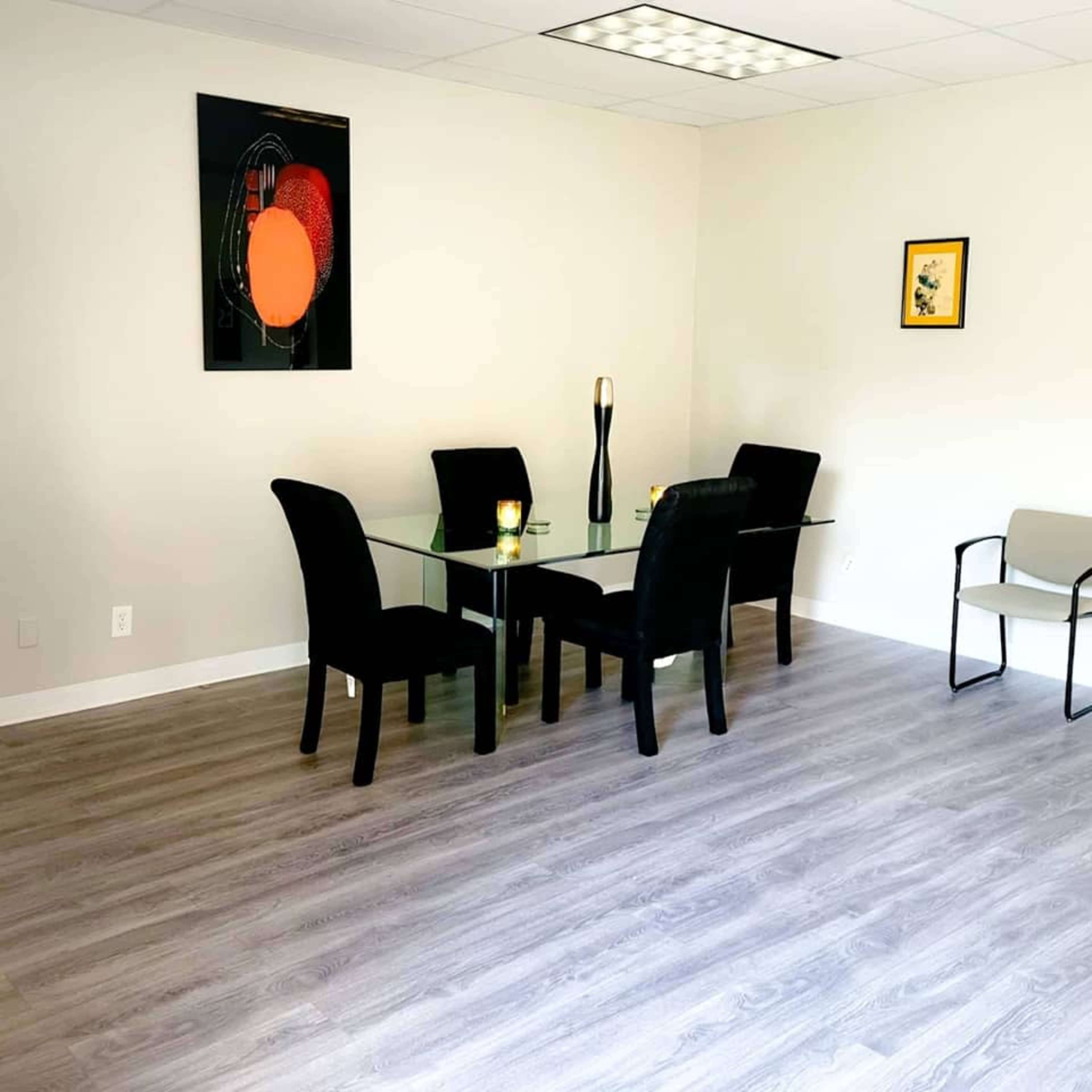 A modern, minimalist room features a glass dining table surrounded by black chairs, with a few decorative items and artwork on the walls.