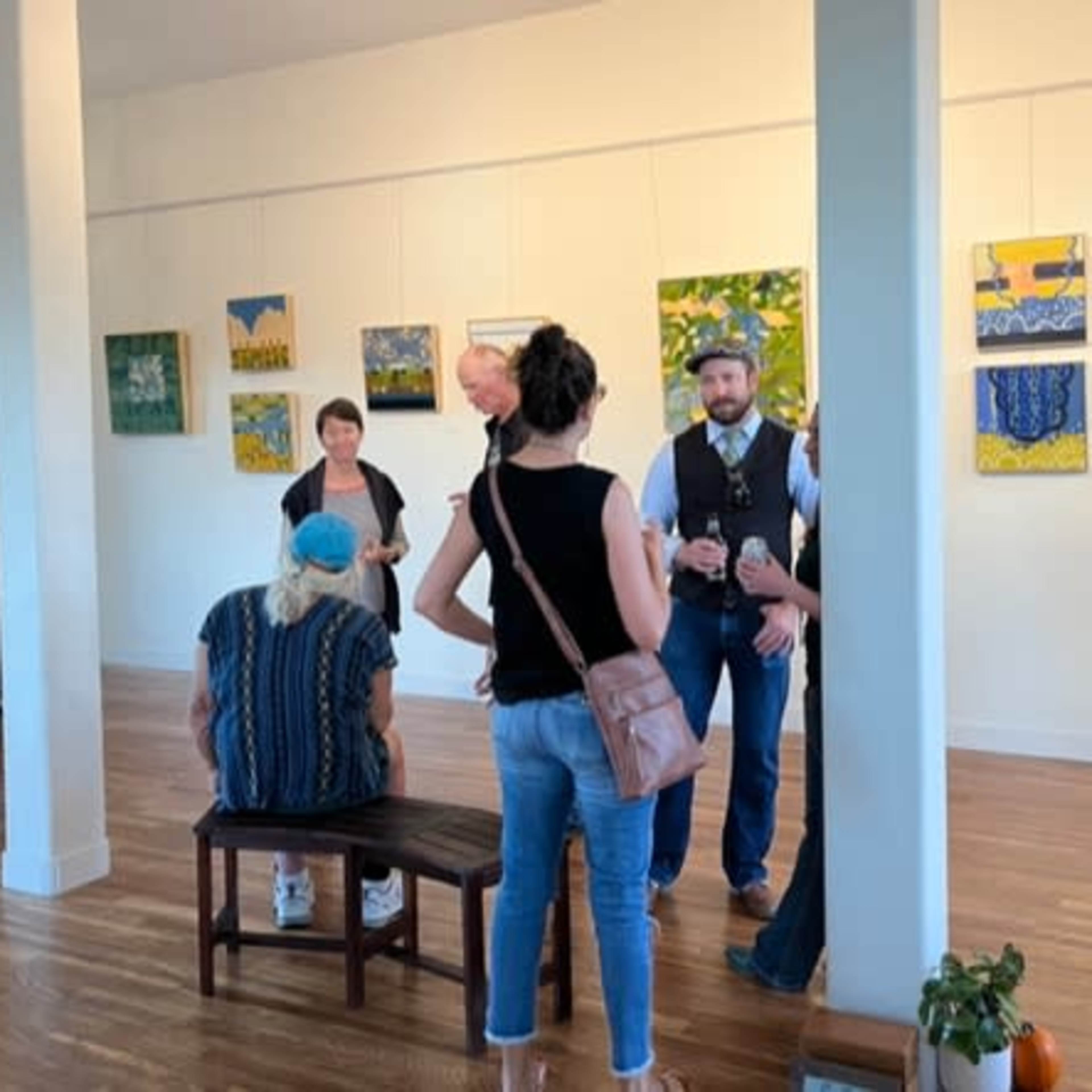 A group of people interacts in an art gallery featuring colorful paintings on the walls.