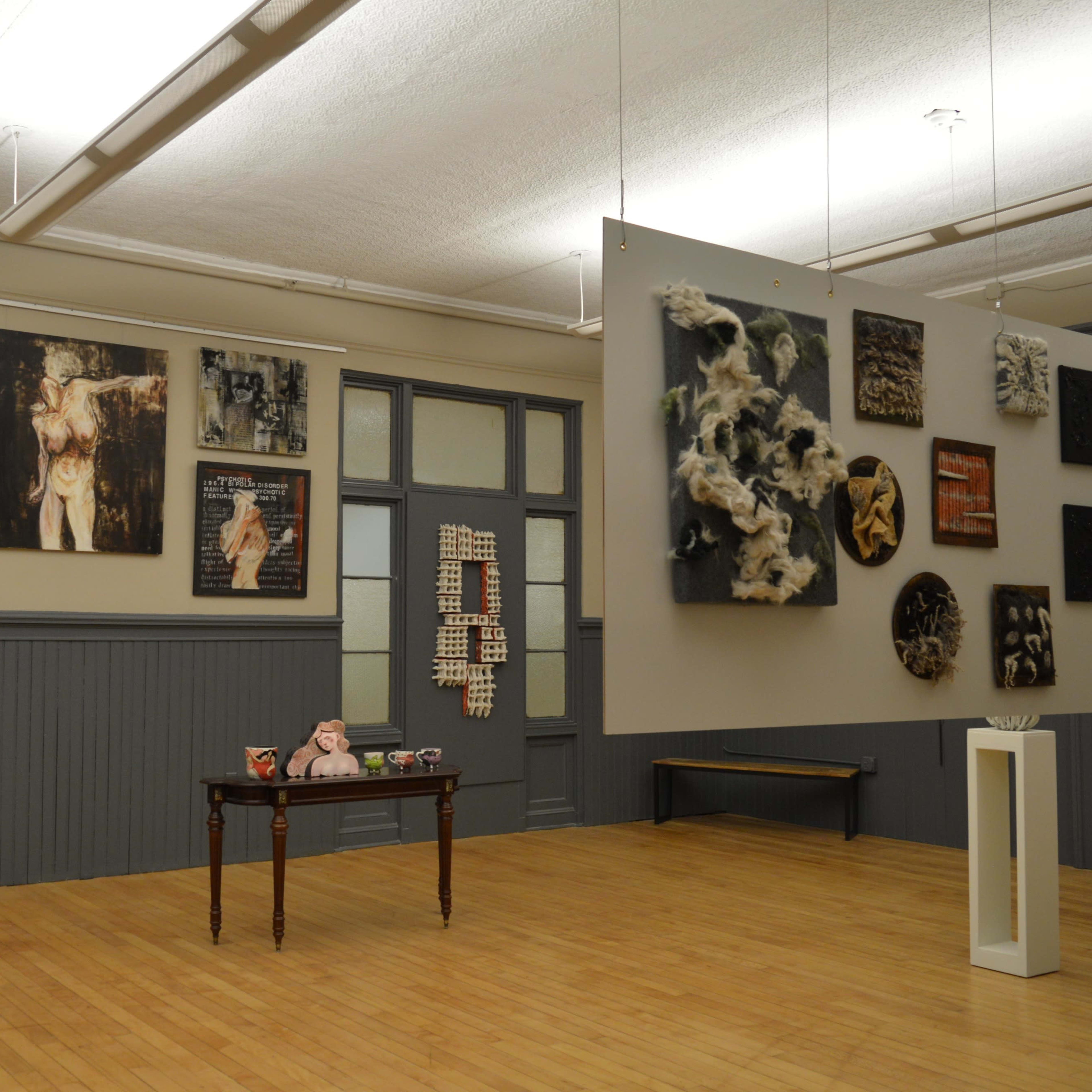 An art gallery featuring a variety of framed artworks on the walls and a small table displaying decorative items in the center.