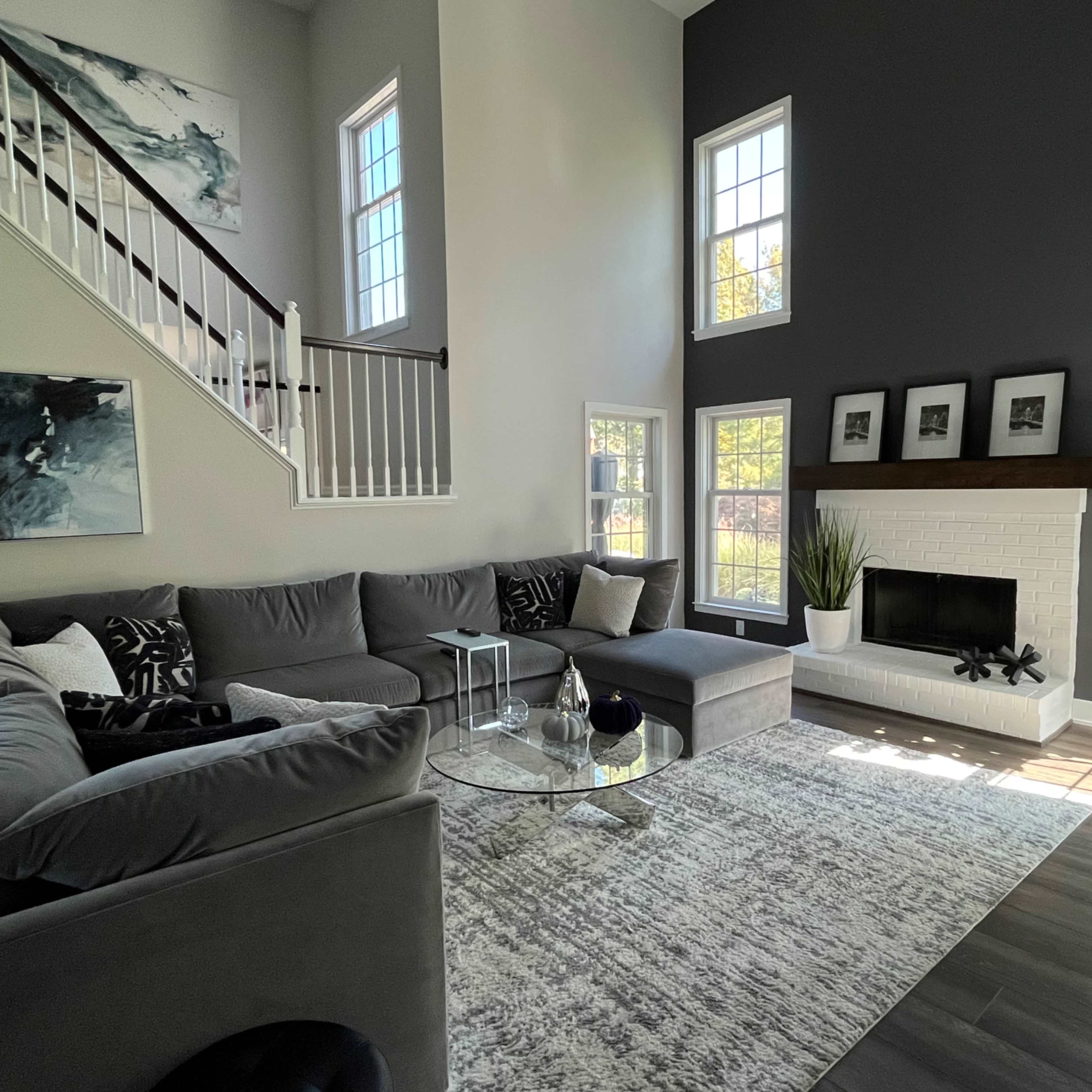 The living room features a large sectional sofa, a round glass coffee table, and a white brick fireplace, with large windows allowing natural light to fill the space.