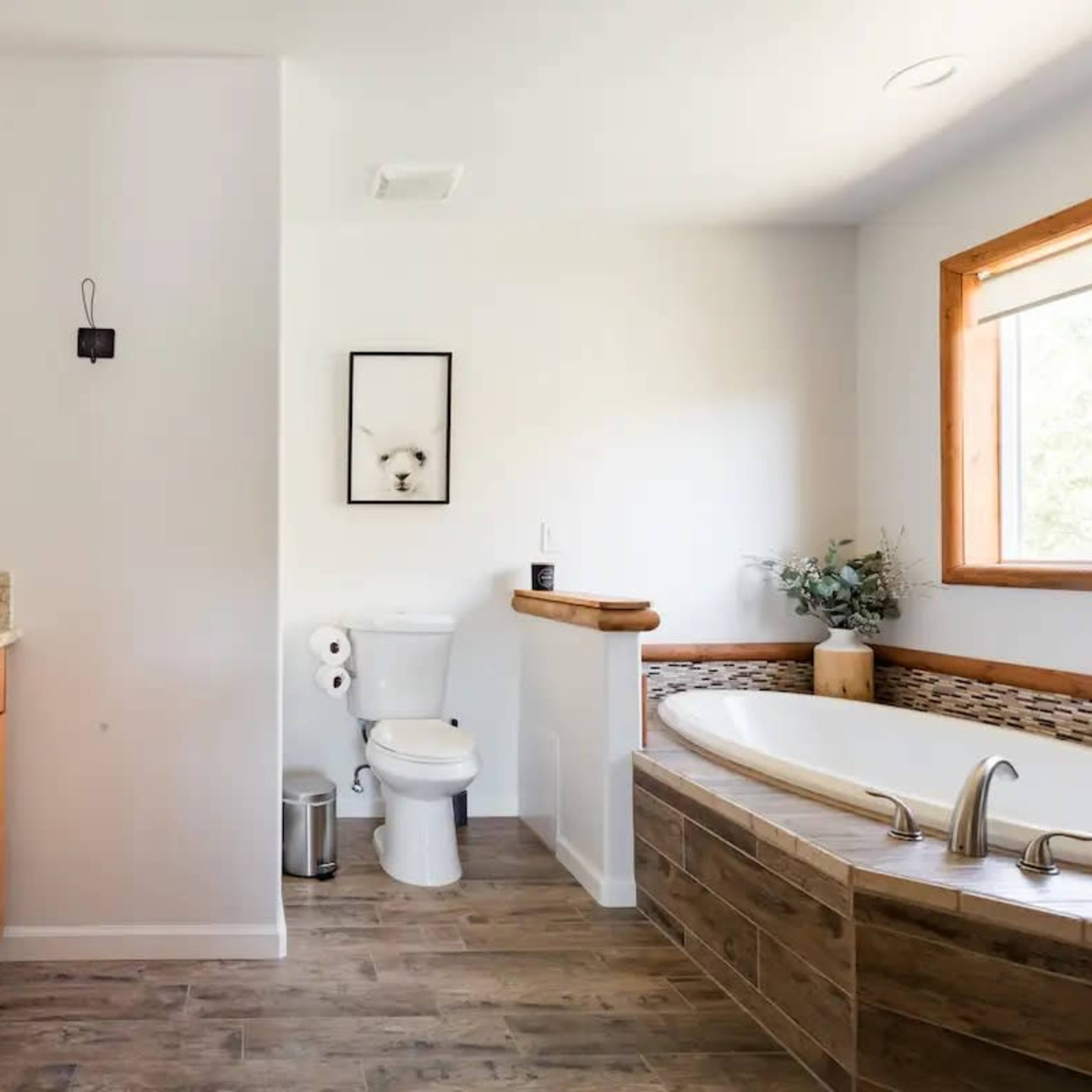 The bathroom features a wooden vanity with a sink, a toilet, a large bathtub, and a window providing natural light.