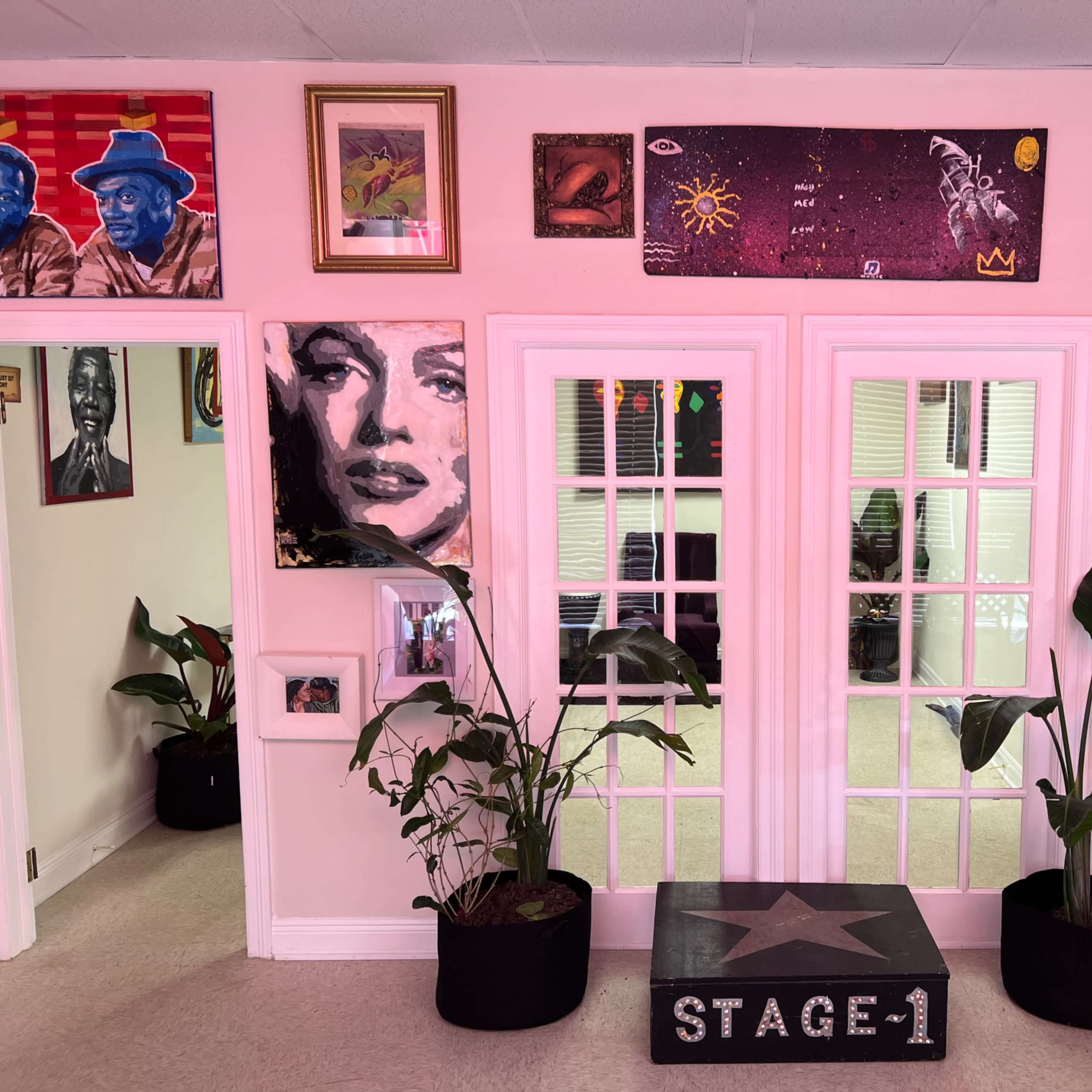 A doorway with glass-paneled double doors surrounded by various framed artworks and plants in two black pots.