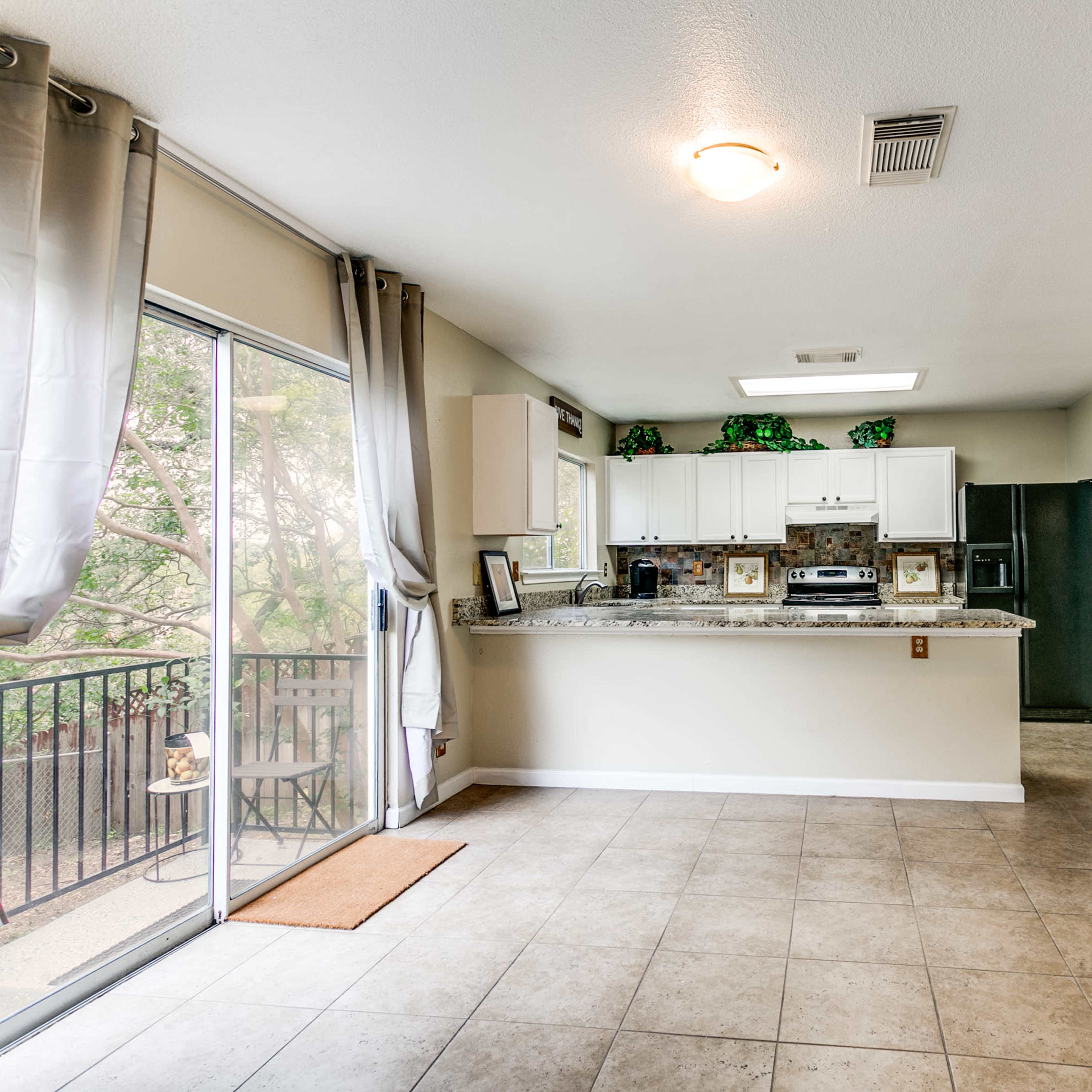 A spacious kitchen area features granite countertops, white cabinets, and large windows overlooking a balcony.