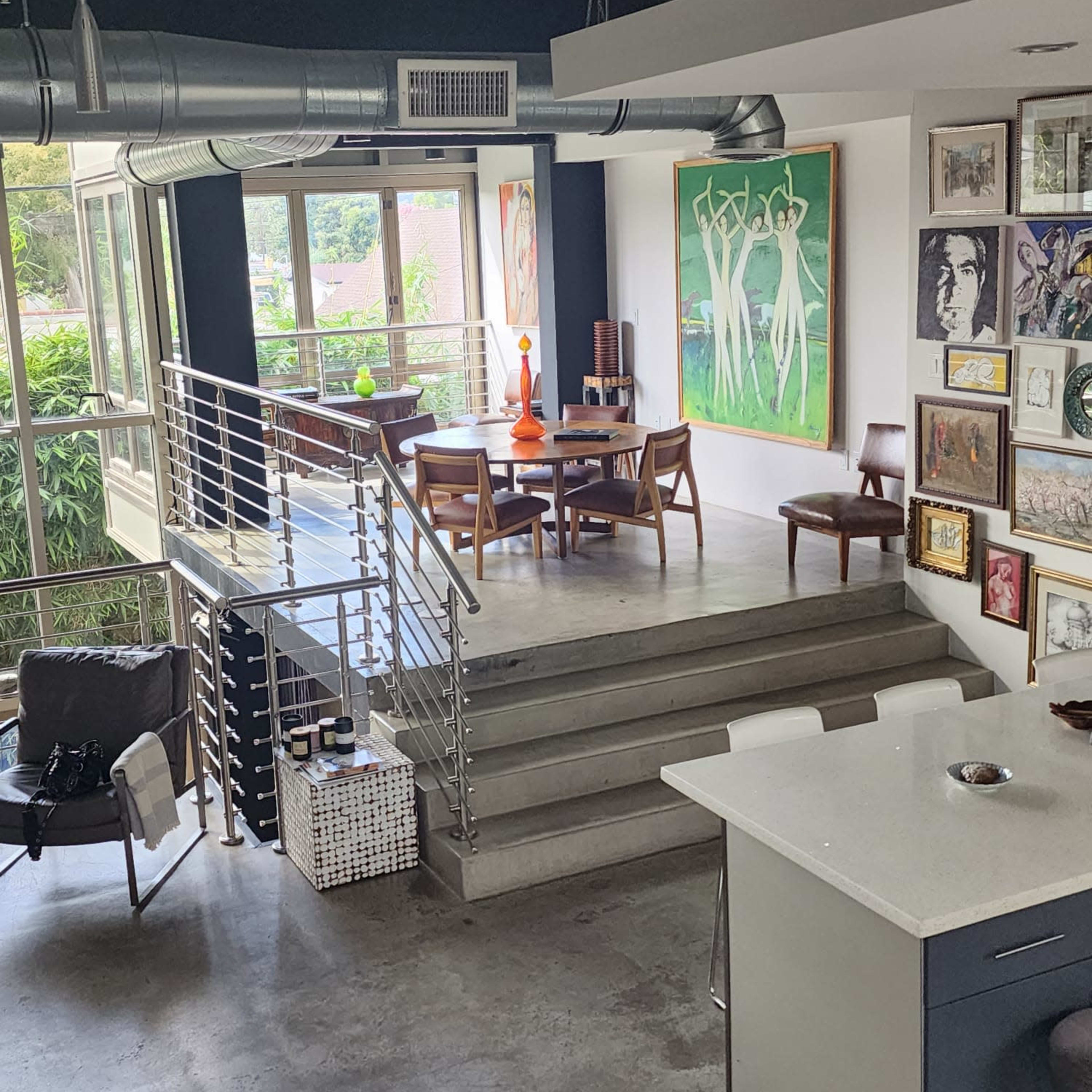 A modern, multi-level living space featuring a dining area with artwork on the walls and large windows overlooking greenery.