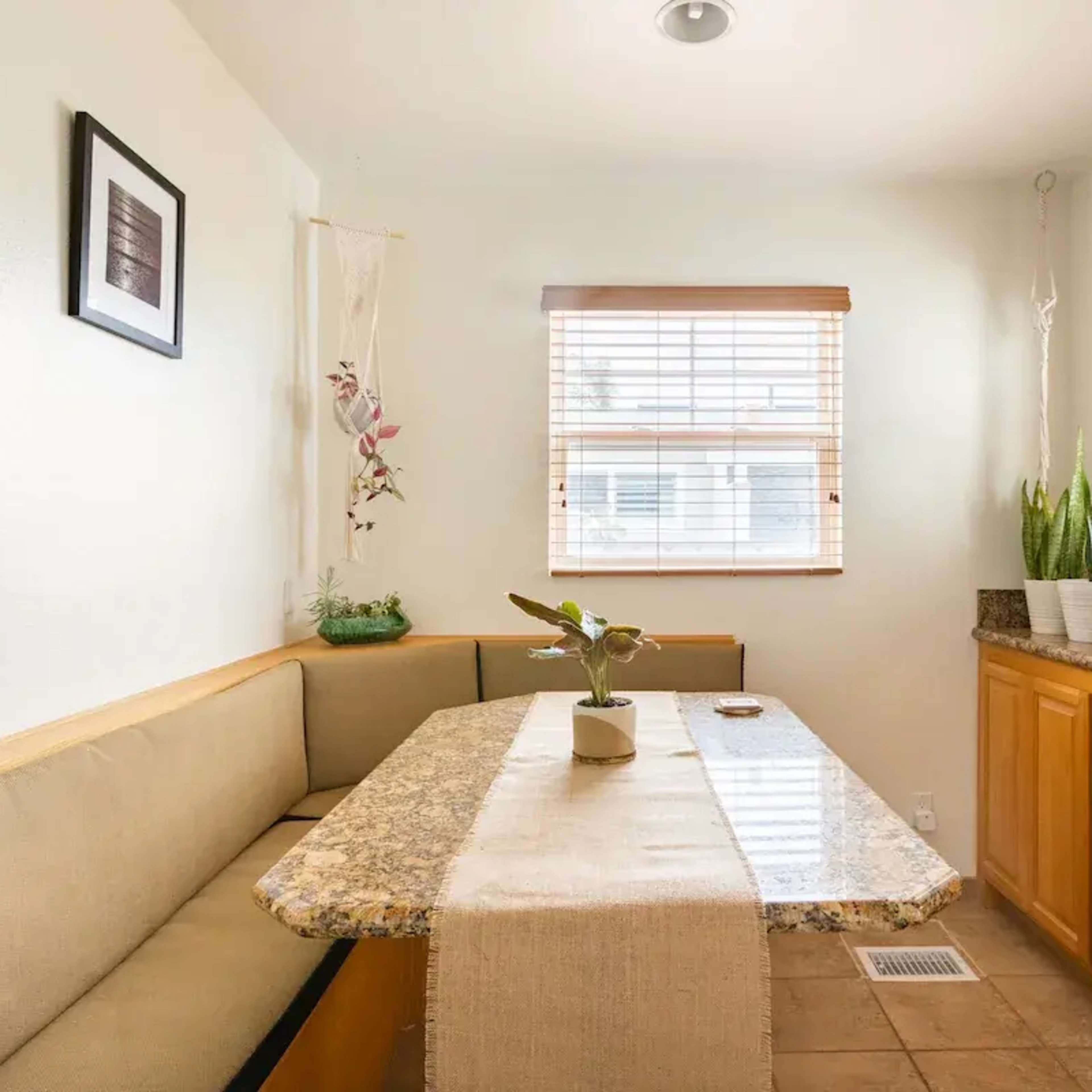 A small dining area features a granite-topped table, a bench along one wall, and plants on the windowsill.