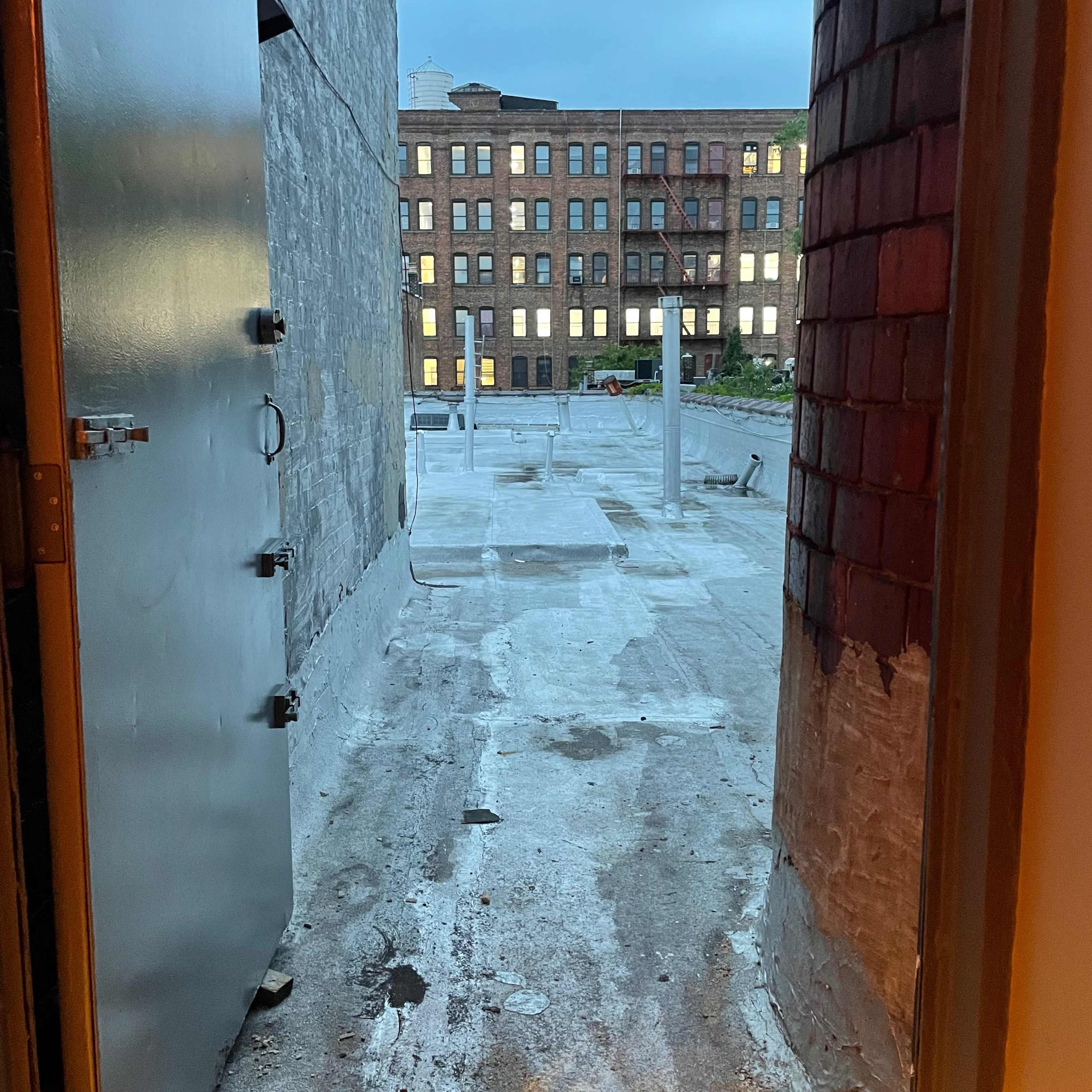 An open door leading to a flat rooftop area with a view of a neighboring brick building.
