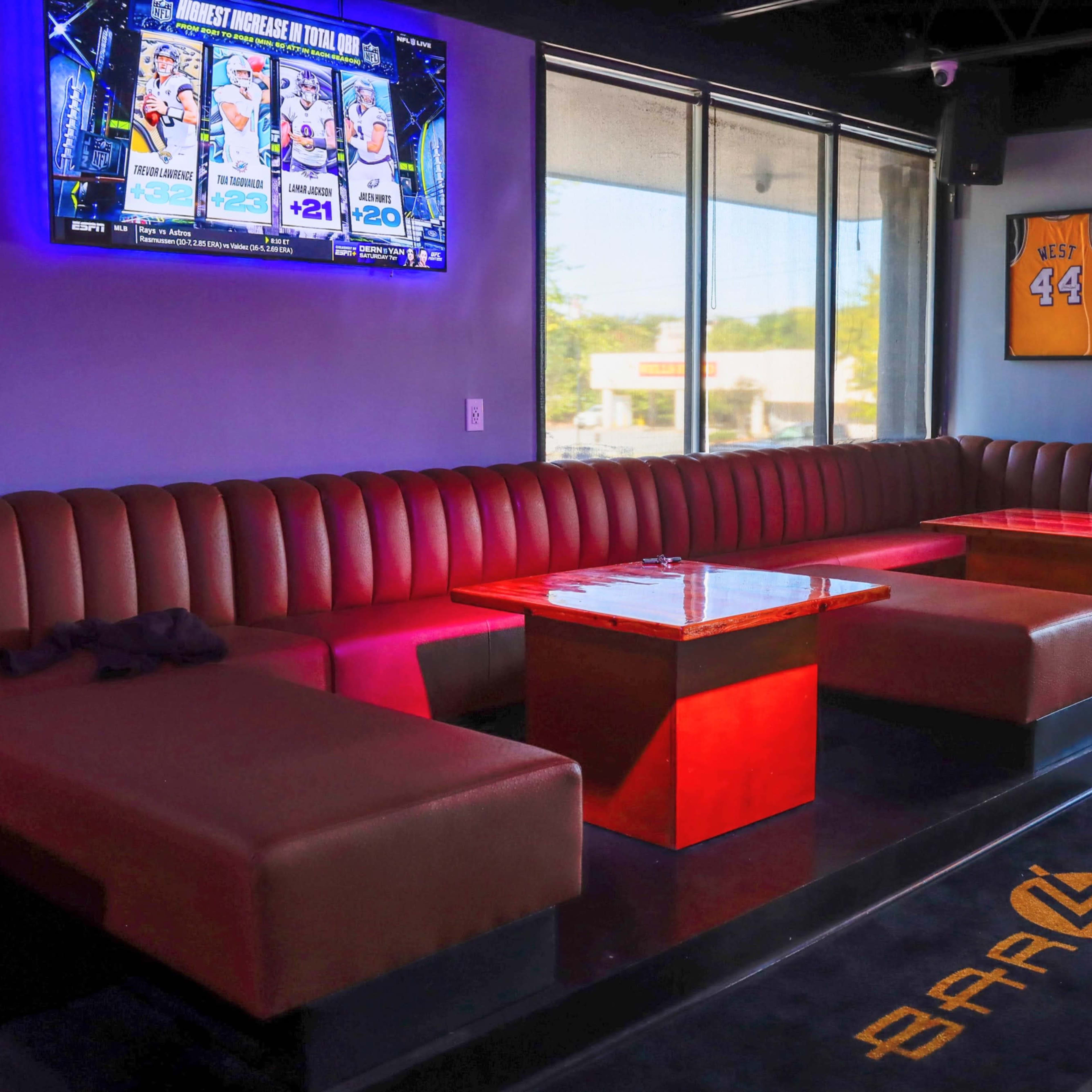 The interior of a lounge features red benches and tables, with a television screen displaying sports content on the wall.
