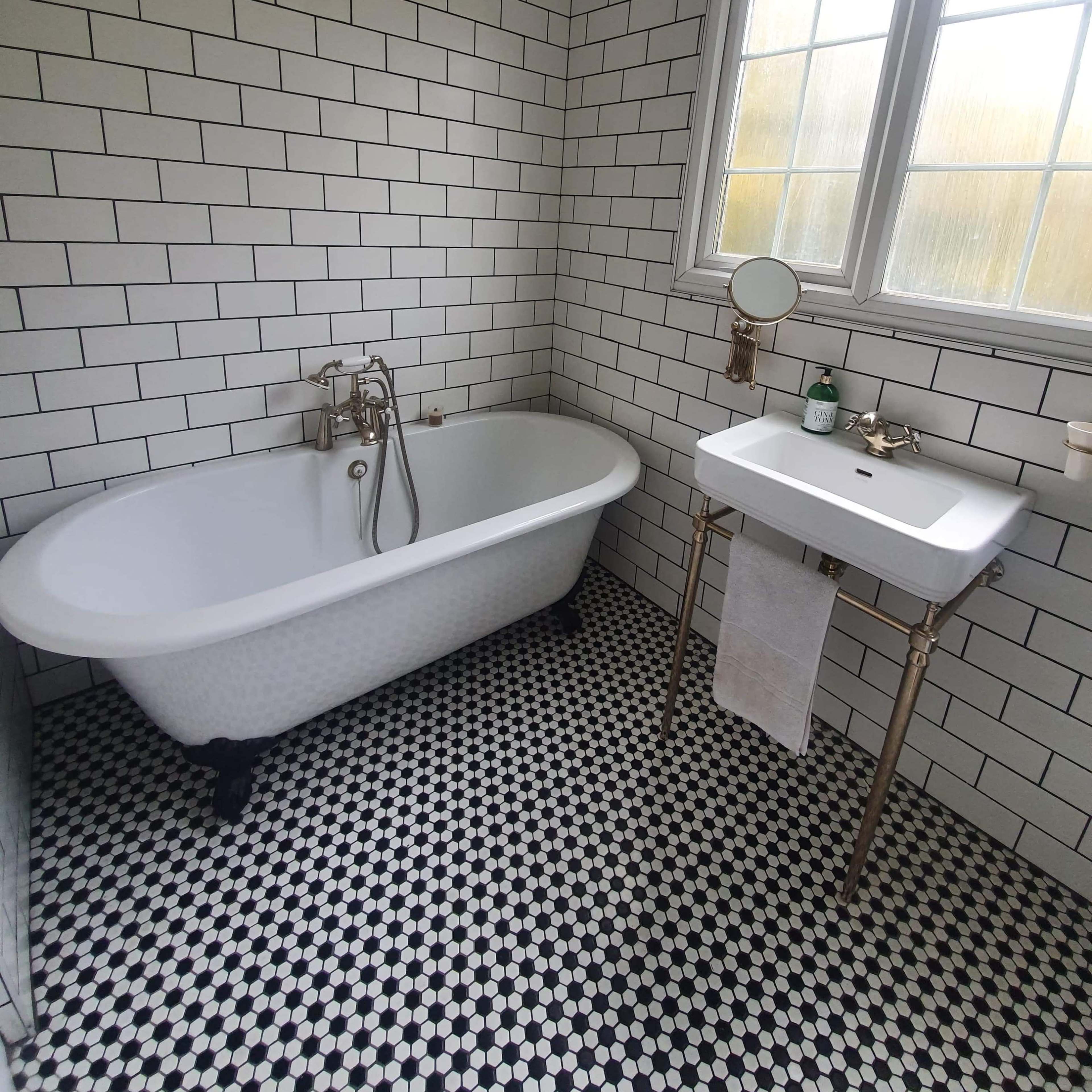 The bathroom features a freestanding white clawfoot tub, a pedestal sink, and black-and-white tiled flooring.