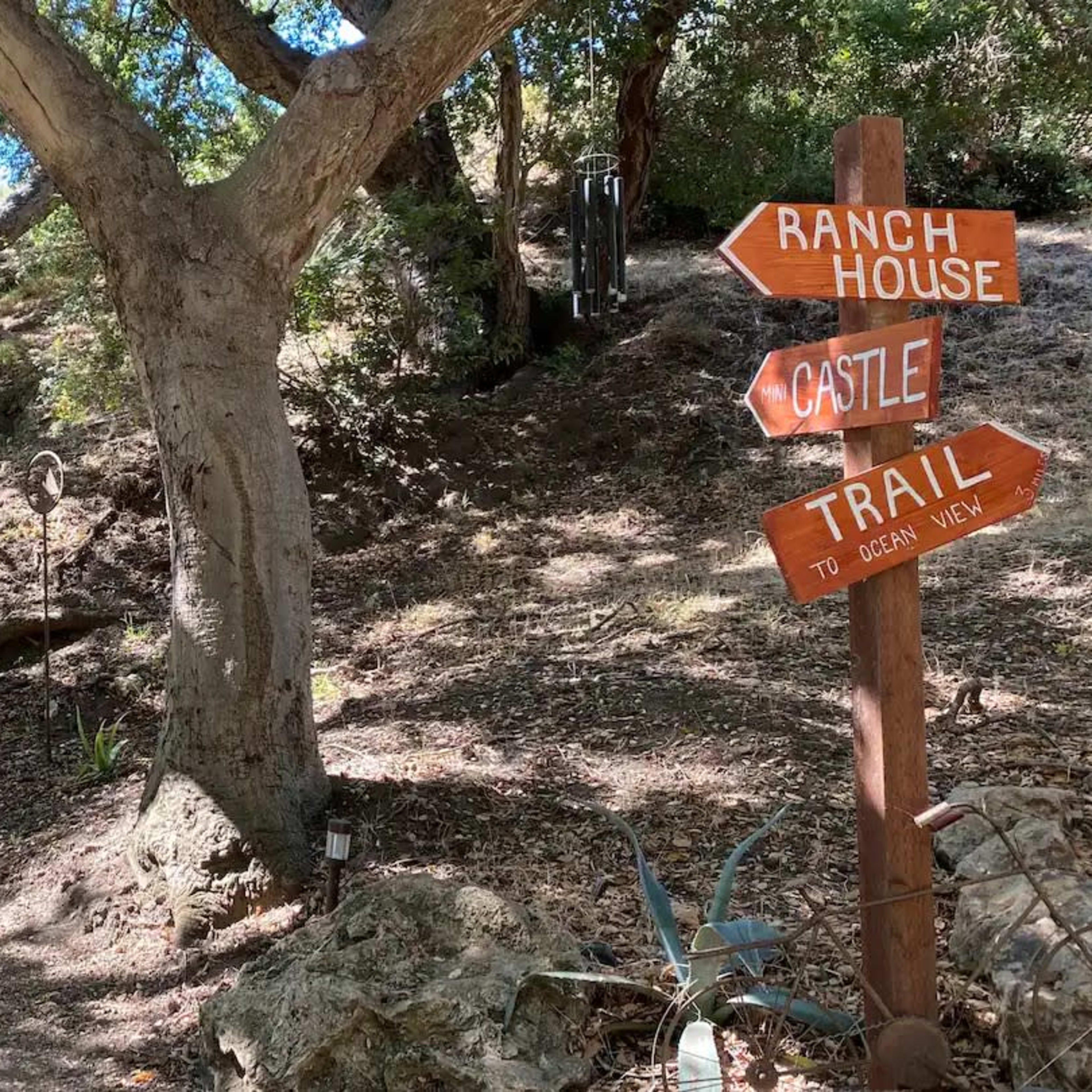 A path leading up a hillside, flanked by trees, with a signpost indicating directions to a ranch house and a castle trail.