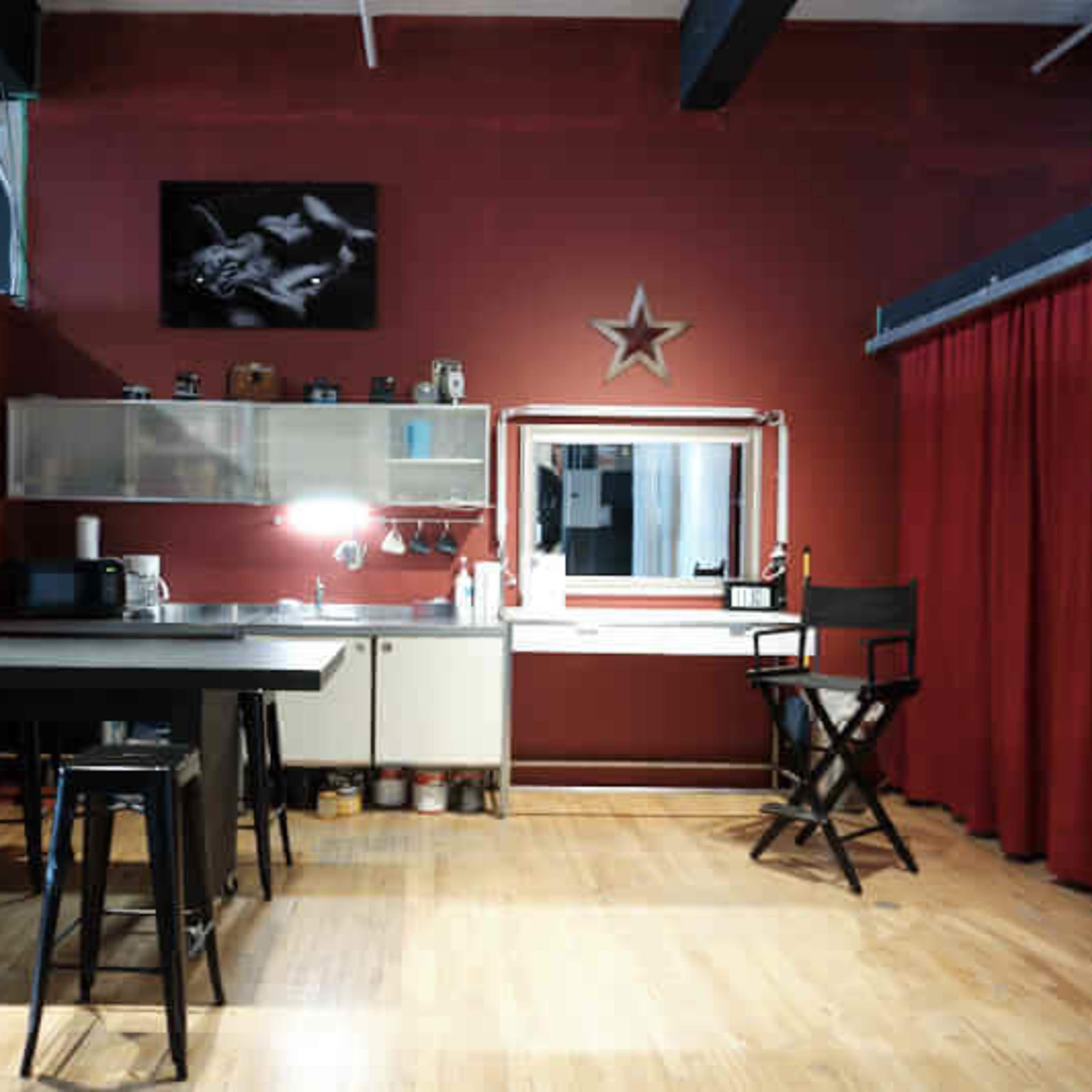 A modern kitchen and workspace area with red walls, a dining table, a microwave, and a large mirror surrounded by a curtain.