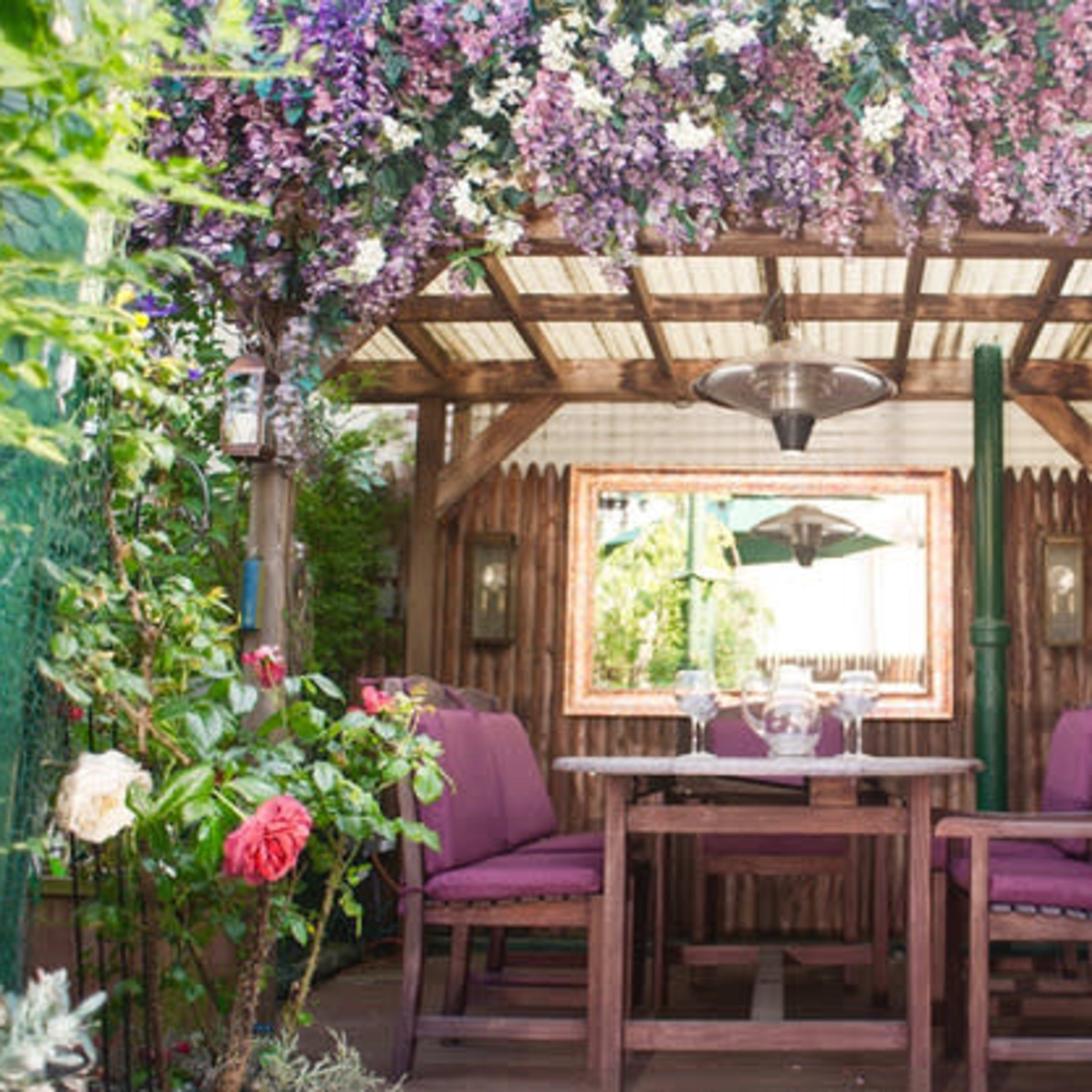A cozy outdoor seating area adorned with purple flowers, featuring a wooden table and chairs under a decorative canopy.