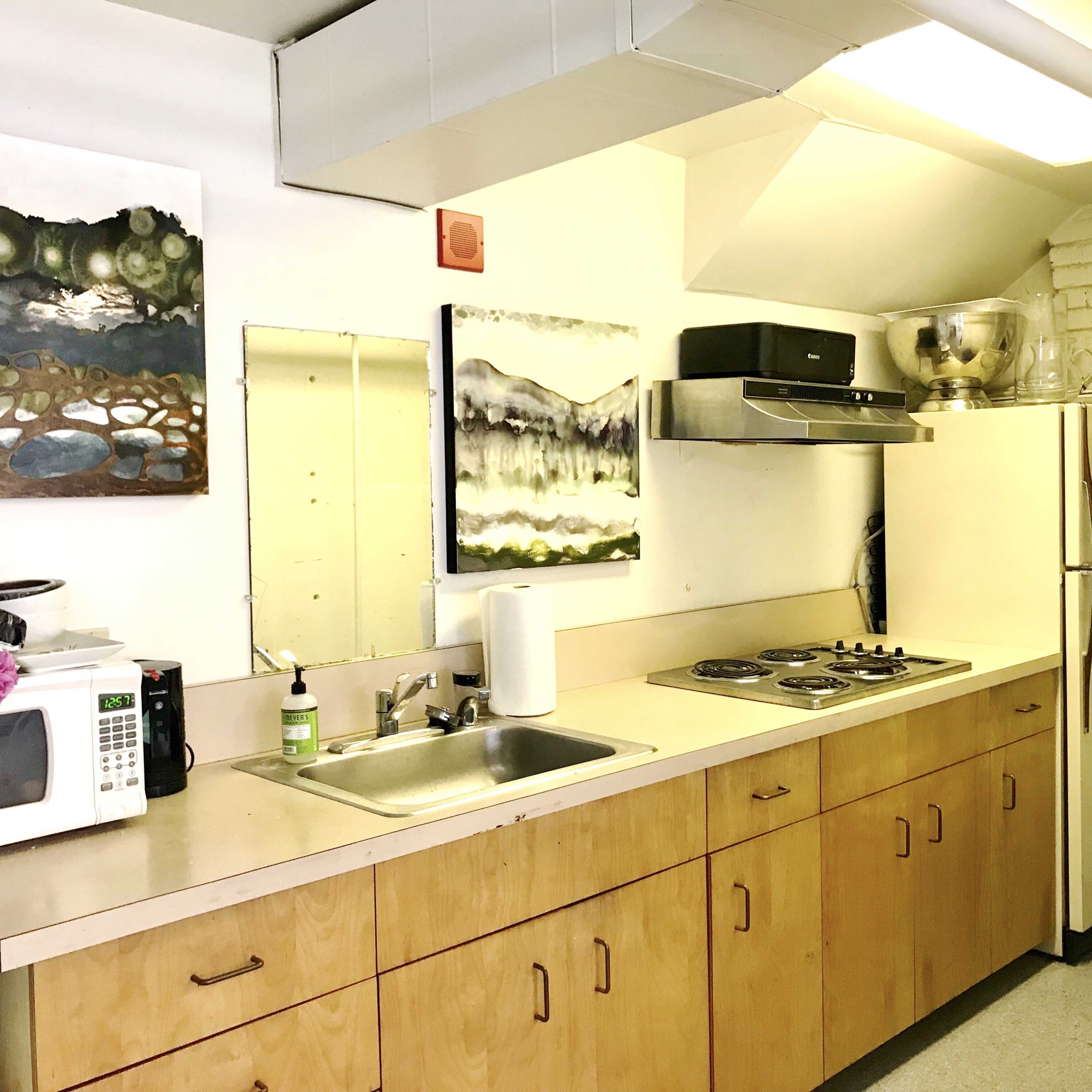 A kitchen with wooden cabinets, a double sink, a stove with four burners, a microwave, and a refrigerator, along with abstract artwork on the walls.
