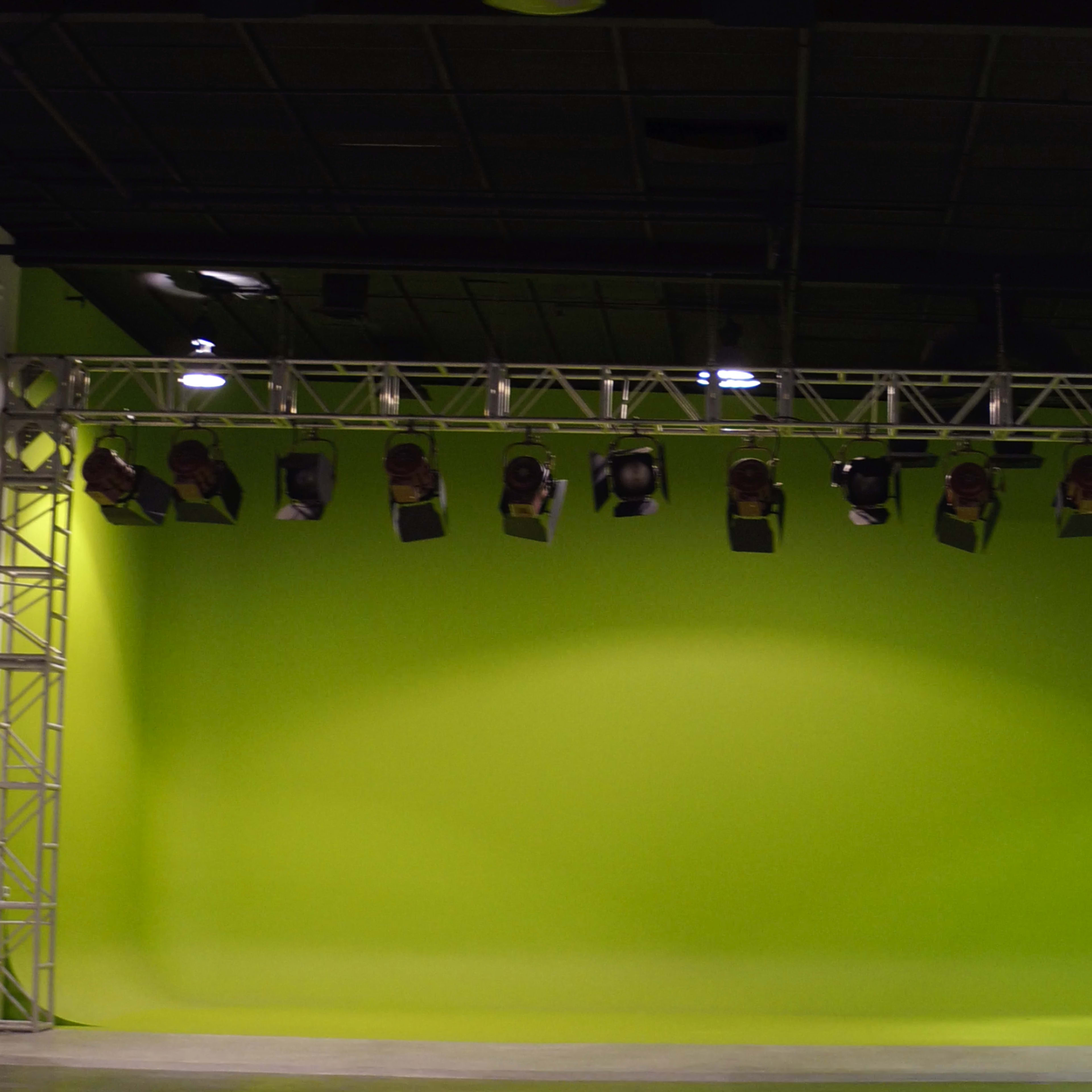 A spacious studio with a bright green backdrop and overhead lights mounted on a metal framework.