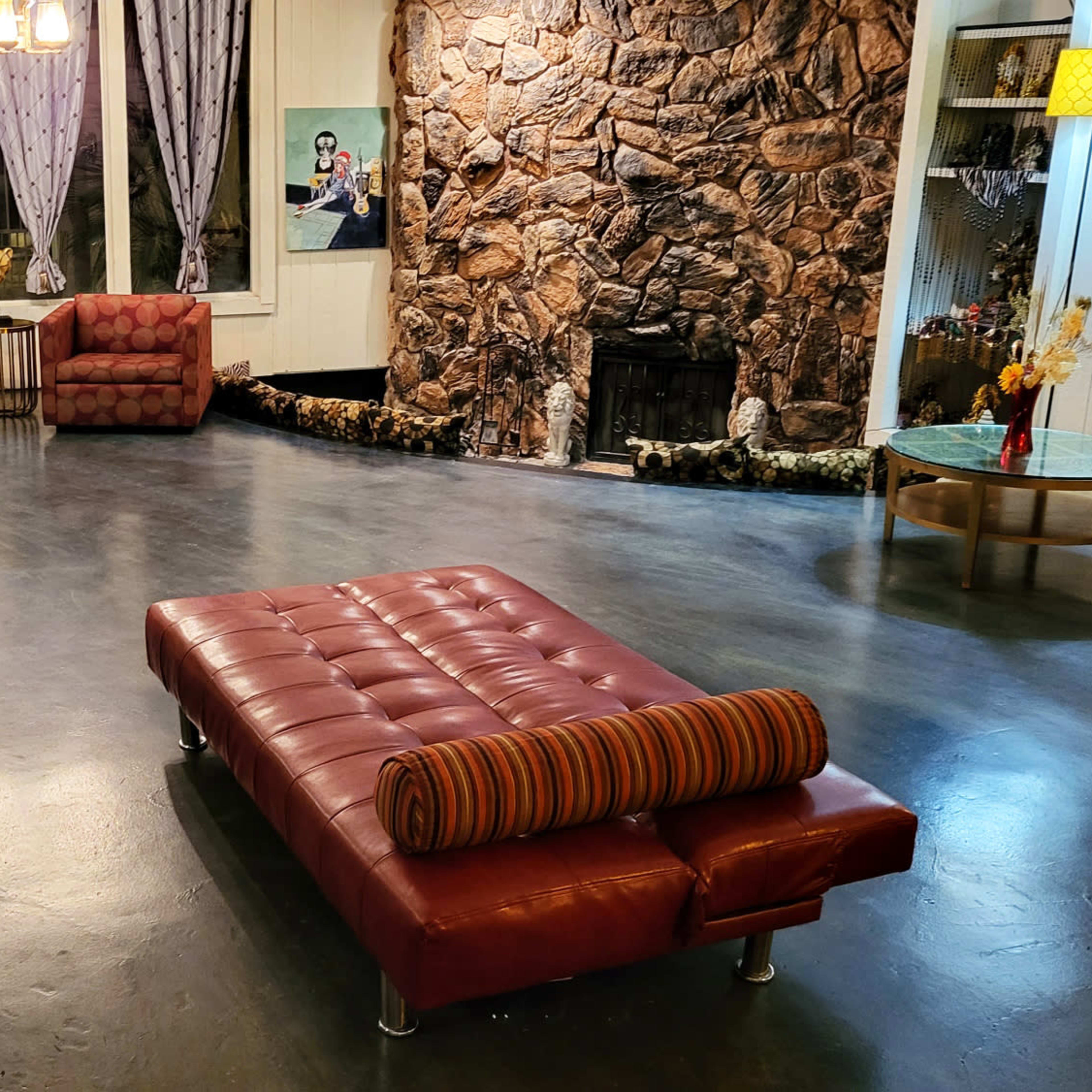 A spacious living area with two red couches, a large stone wall, a fireplace, and a glass coffee table surrounded by a polished floor.