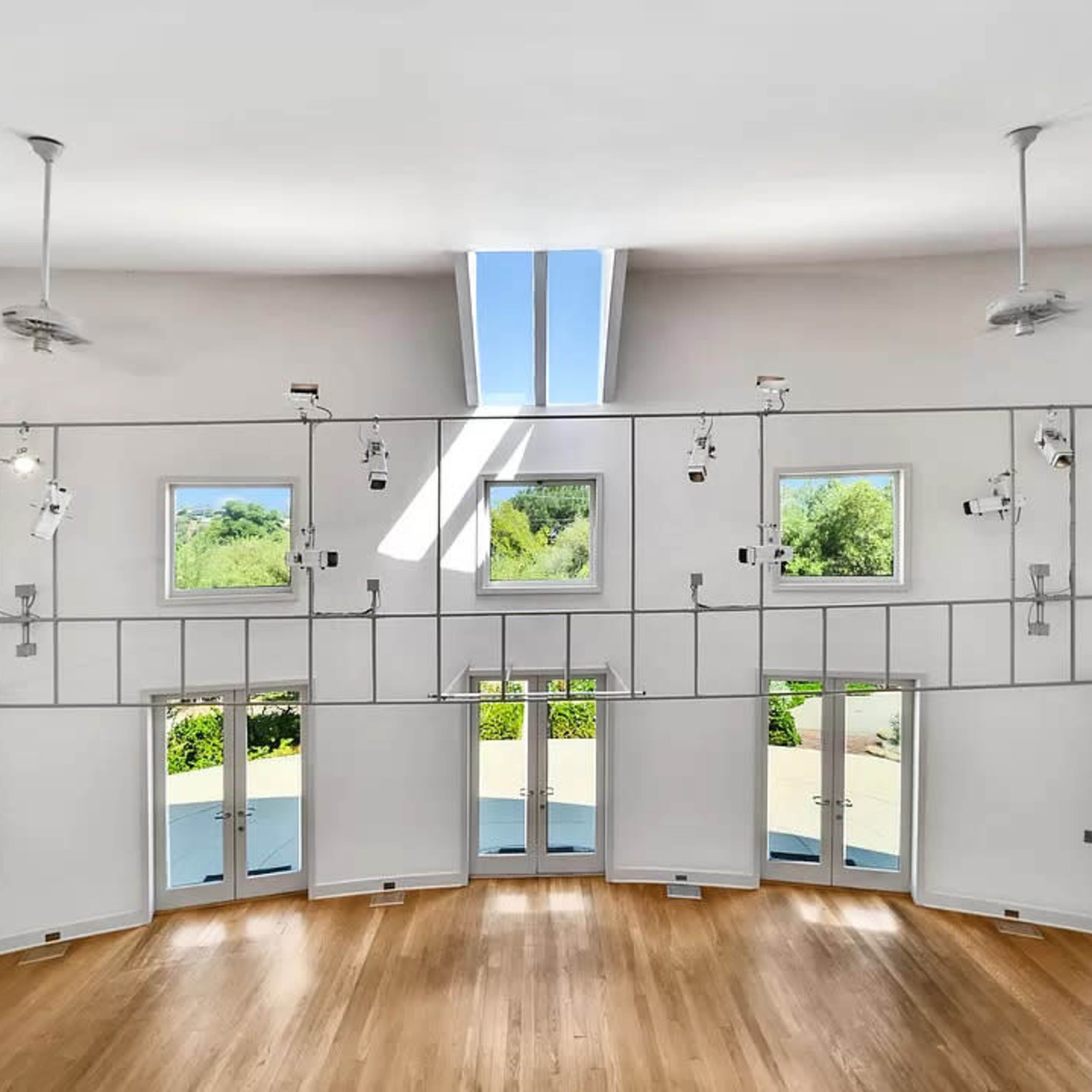 The interior features a circular room with multiple windows and doors, allowing natural light to illuminate the wooden floor.