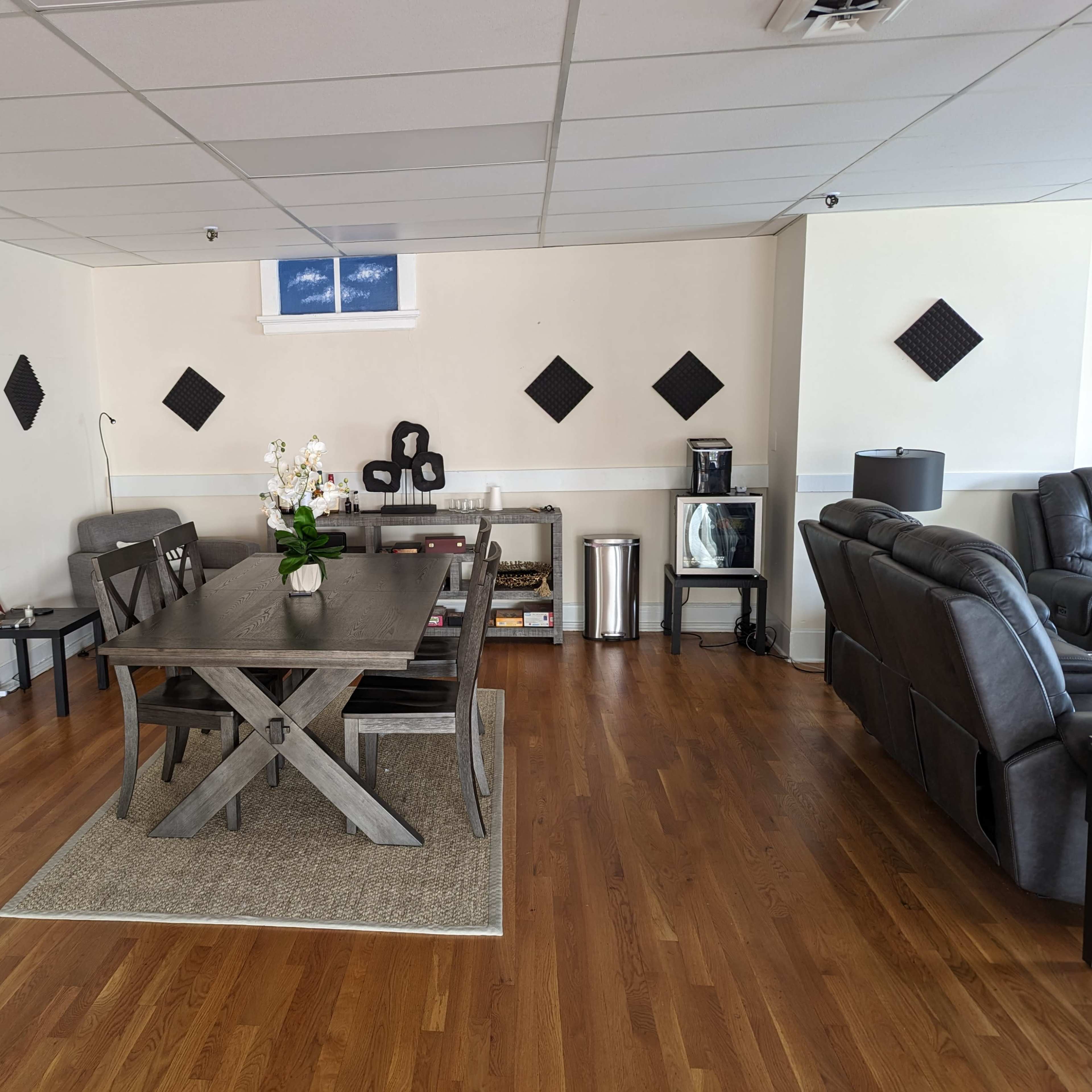 A spacious room featuring a wooden dining table, black leather seating, and decorative wall panels arranged in a geometric pattern.