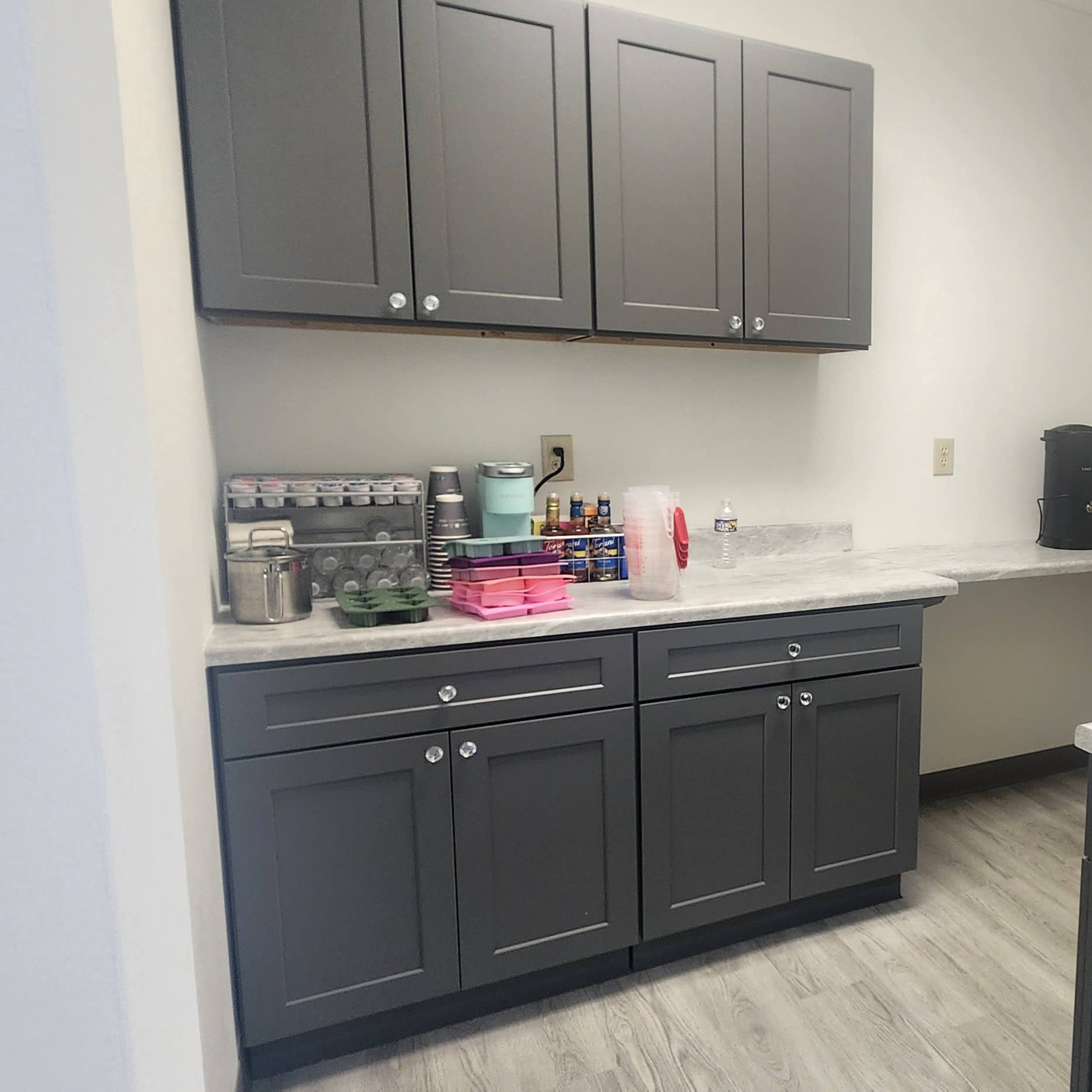 A clean kitchen space features gray cabinetry, a countertop with a coffee maker, and an adjacent sink area.