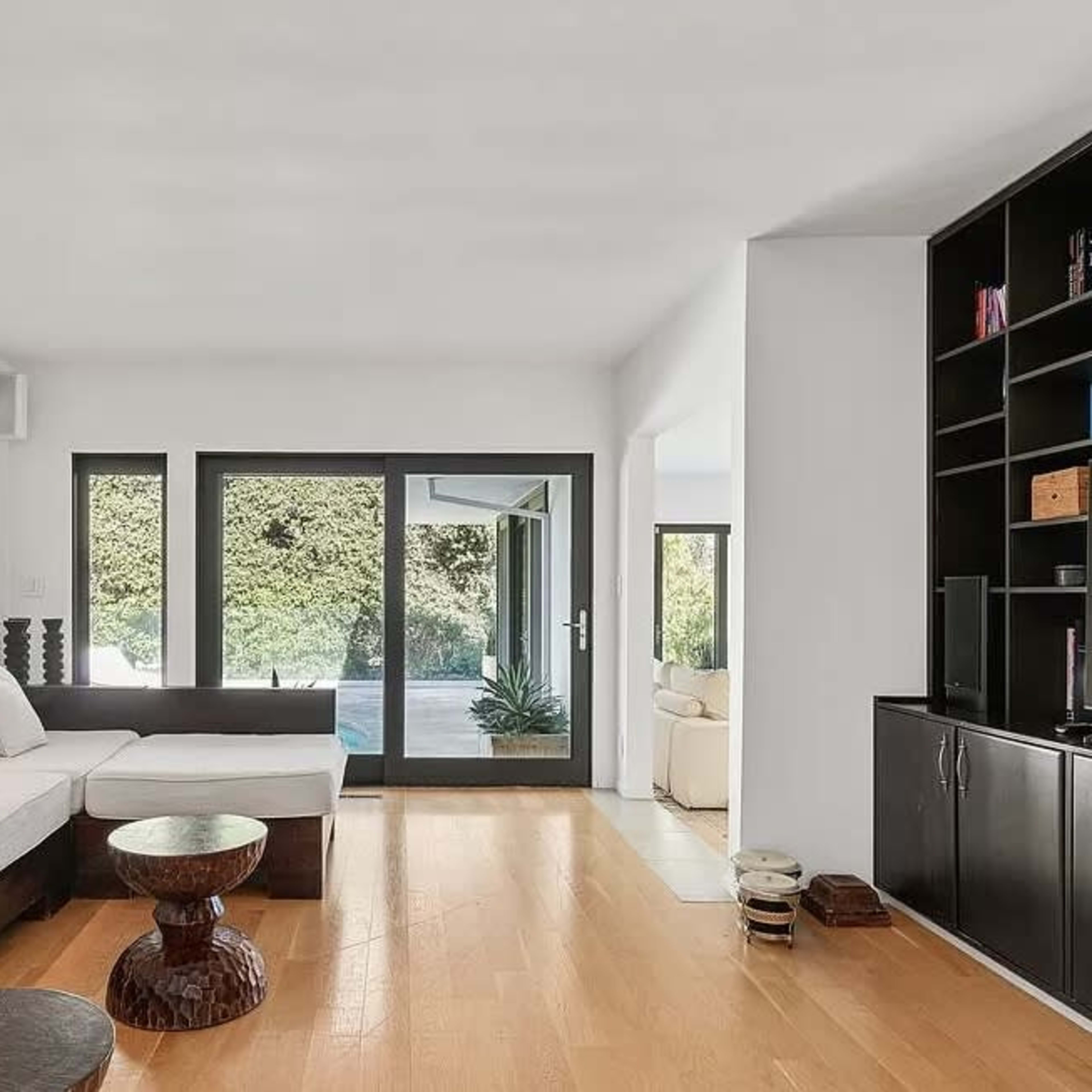 A modern living room features a white sectional sofa, a dark wood coffee table, and large windows overlooking a patio area.
