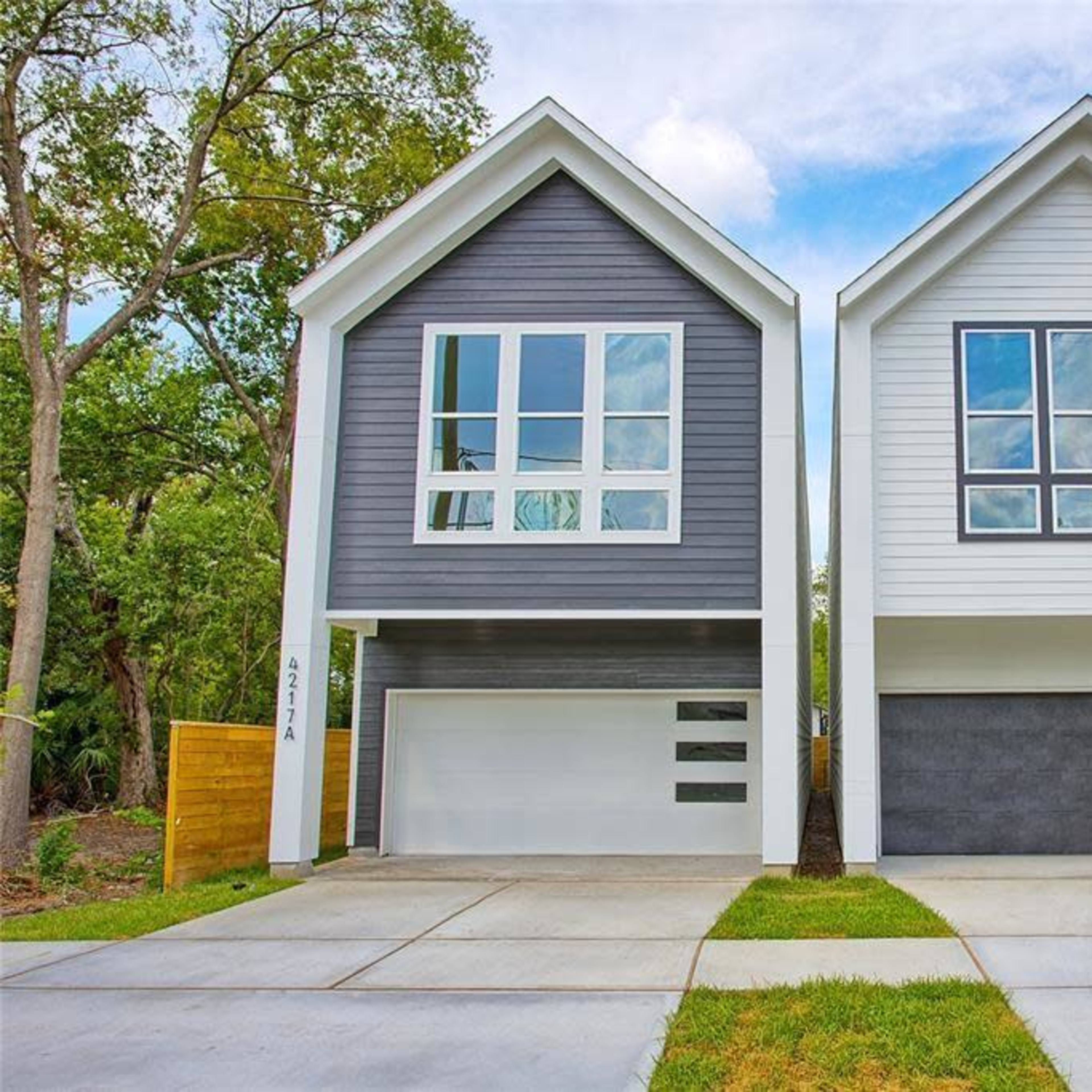 Two modern houses with distinct exterior colors and large windows, situated side by side on a paved driveway.