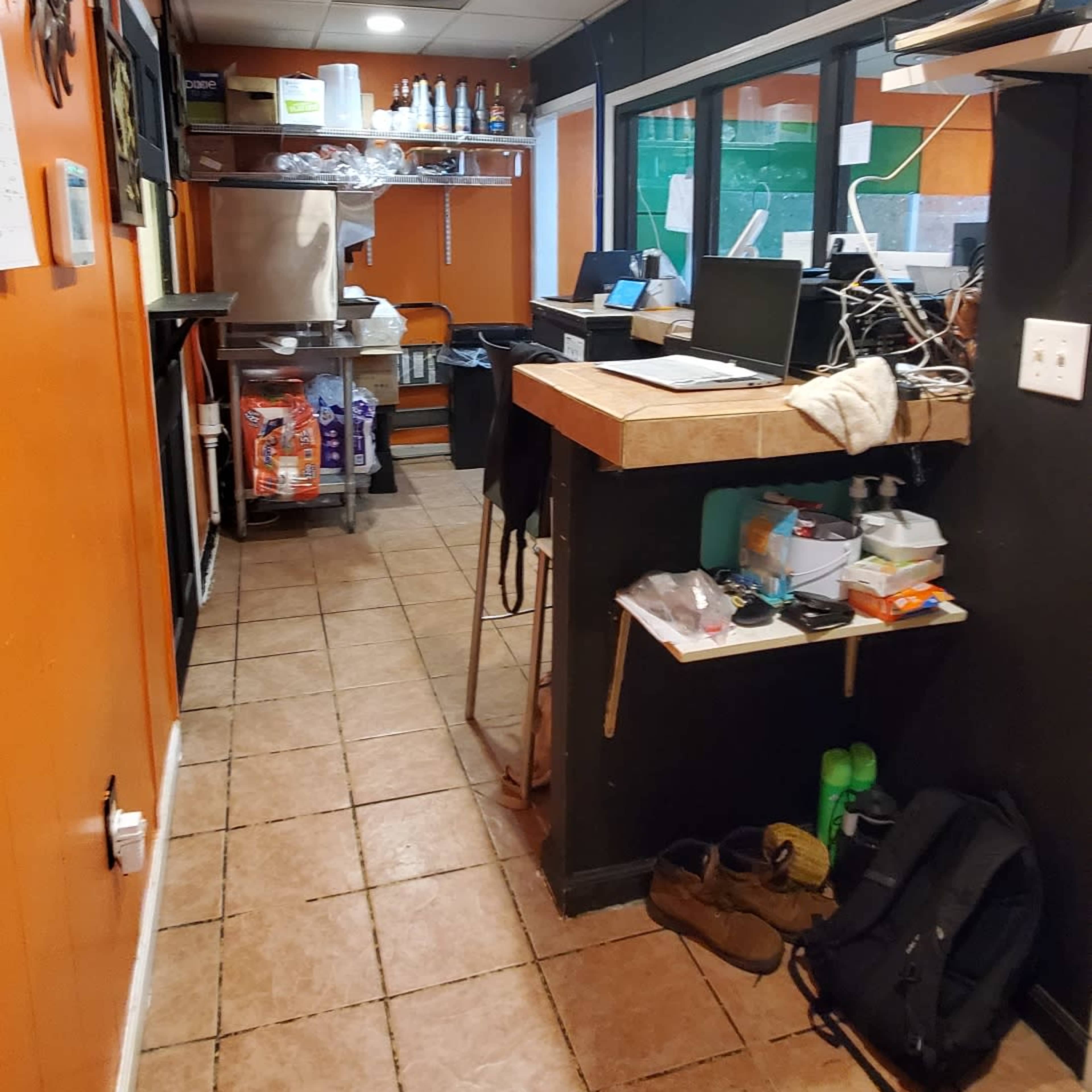 A narrow hallway in a restaurant features an orange and black color scheme, with a counter on the right and shelves stocked with various items.
