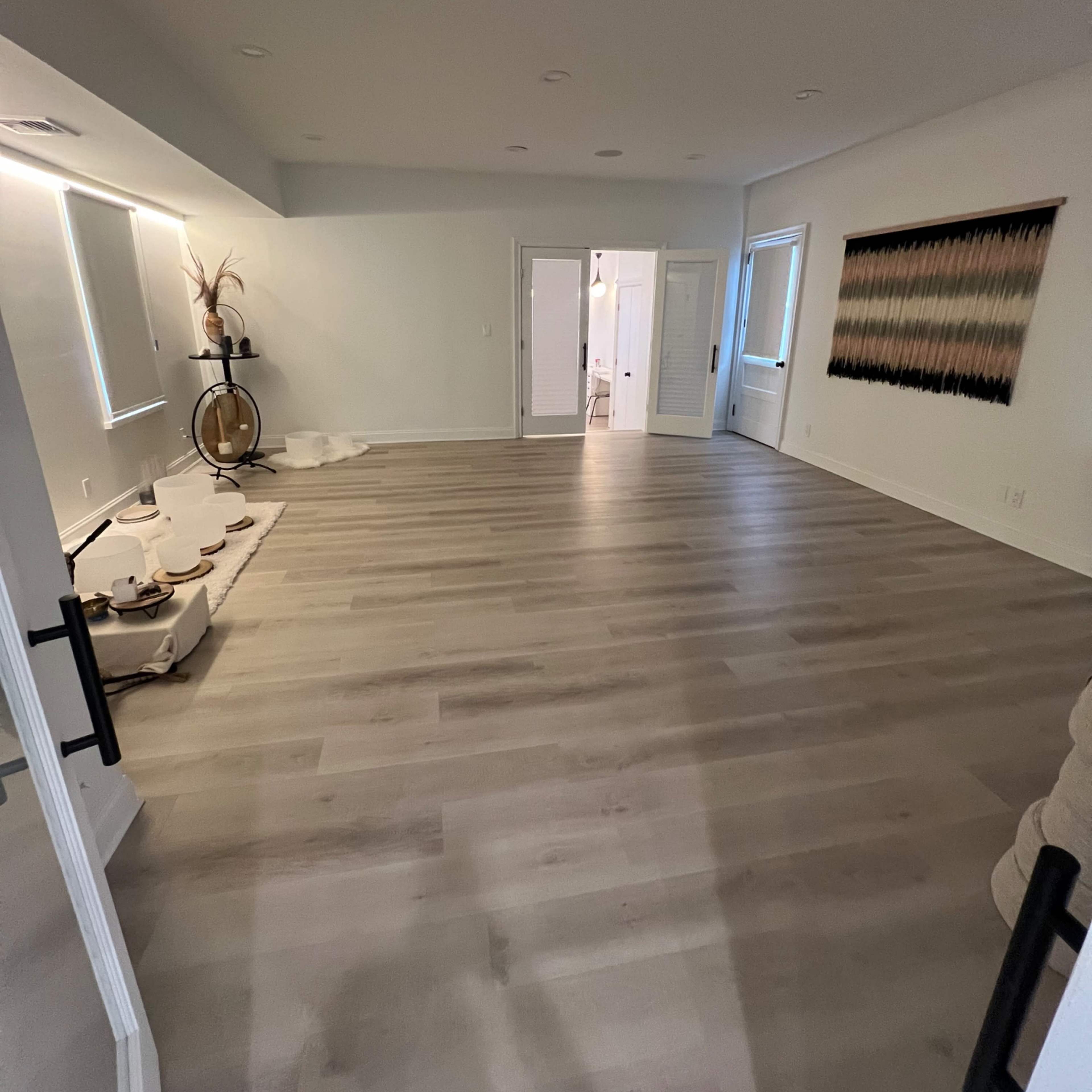 A spacious, empty room with light wood flooring and two doors leading to adjacent areas.