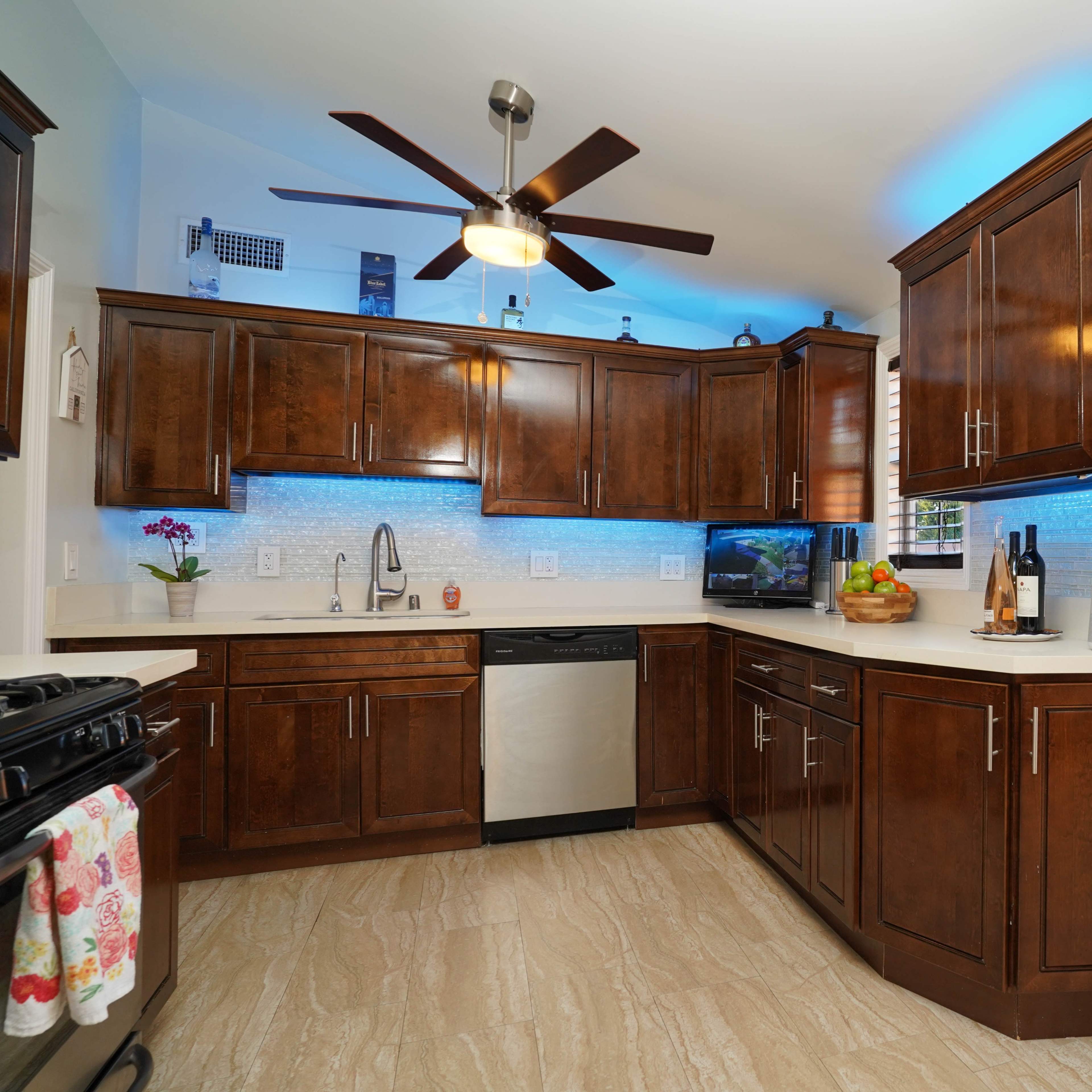 A modern kitchen features dark wooden cabinets, a stainless steel dishwasher, and colorful LED backlighting under the cabinets.